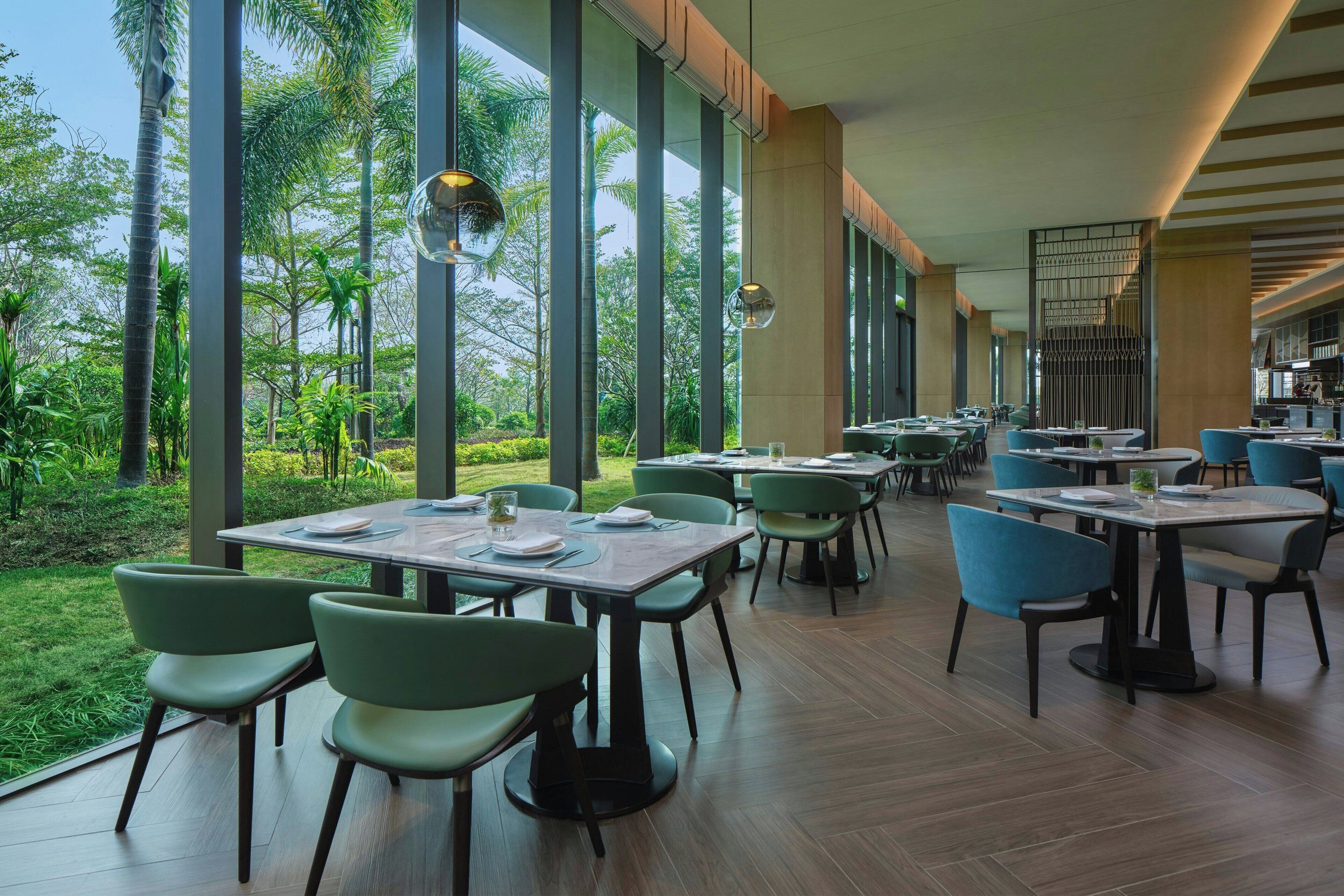 A restaurant with large windows, green chairs, and a view of the outdoors.