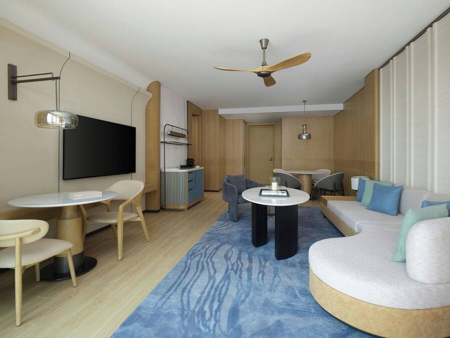 Una sala de estar moderna con un sofá redondo, una mesa de centro, un televisor montado en la pared y un ventilador de techo.