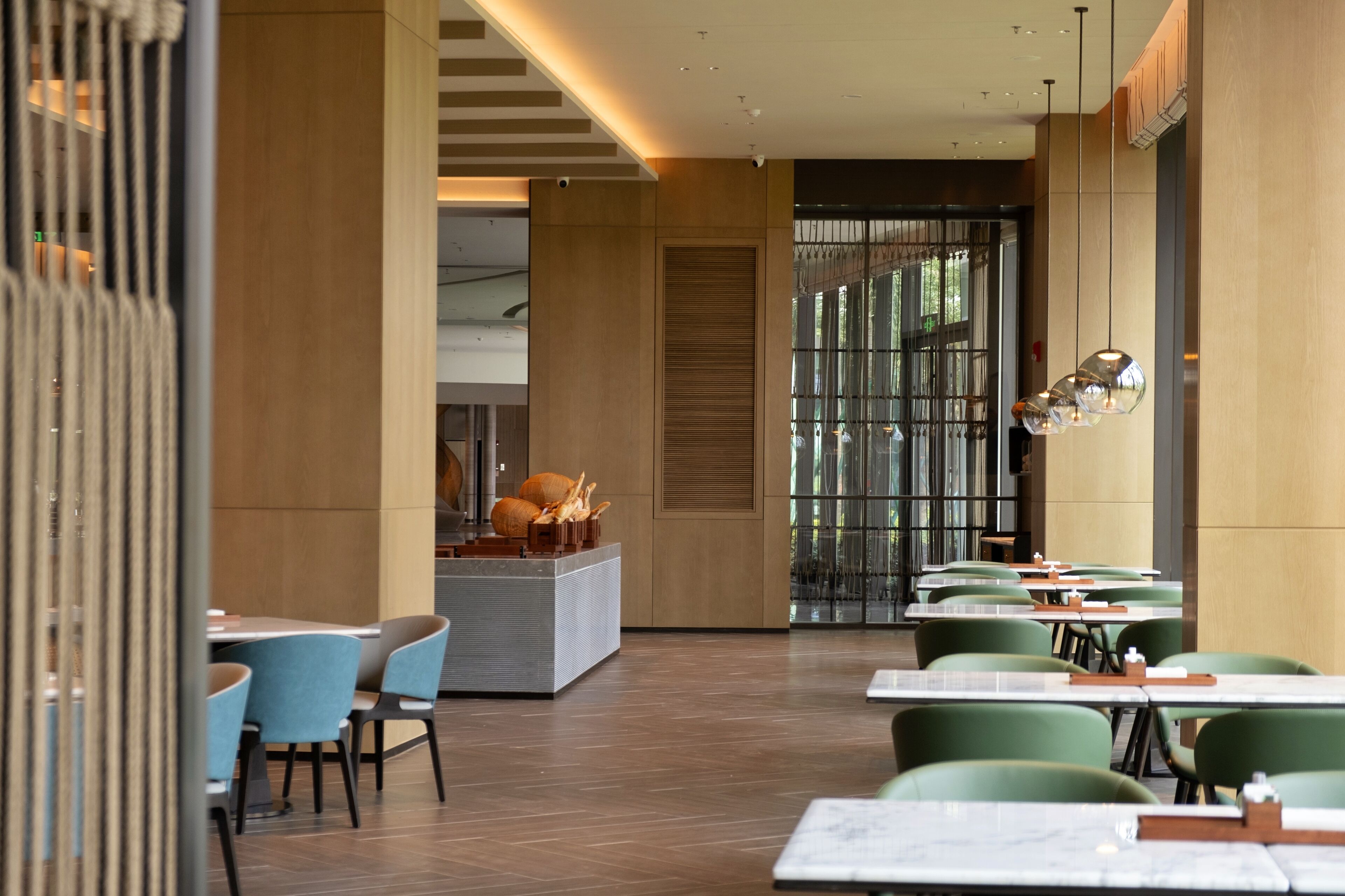 A modern restaurant with a central island, green chairs, and a mix of natural and artificial lighting.