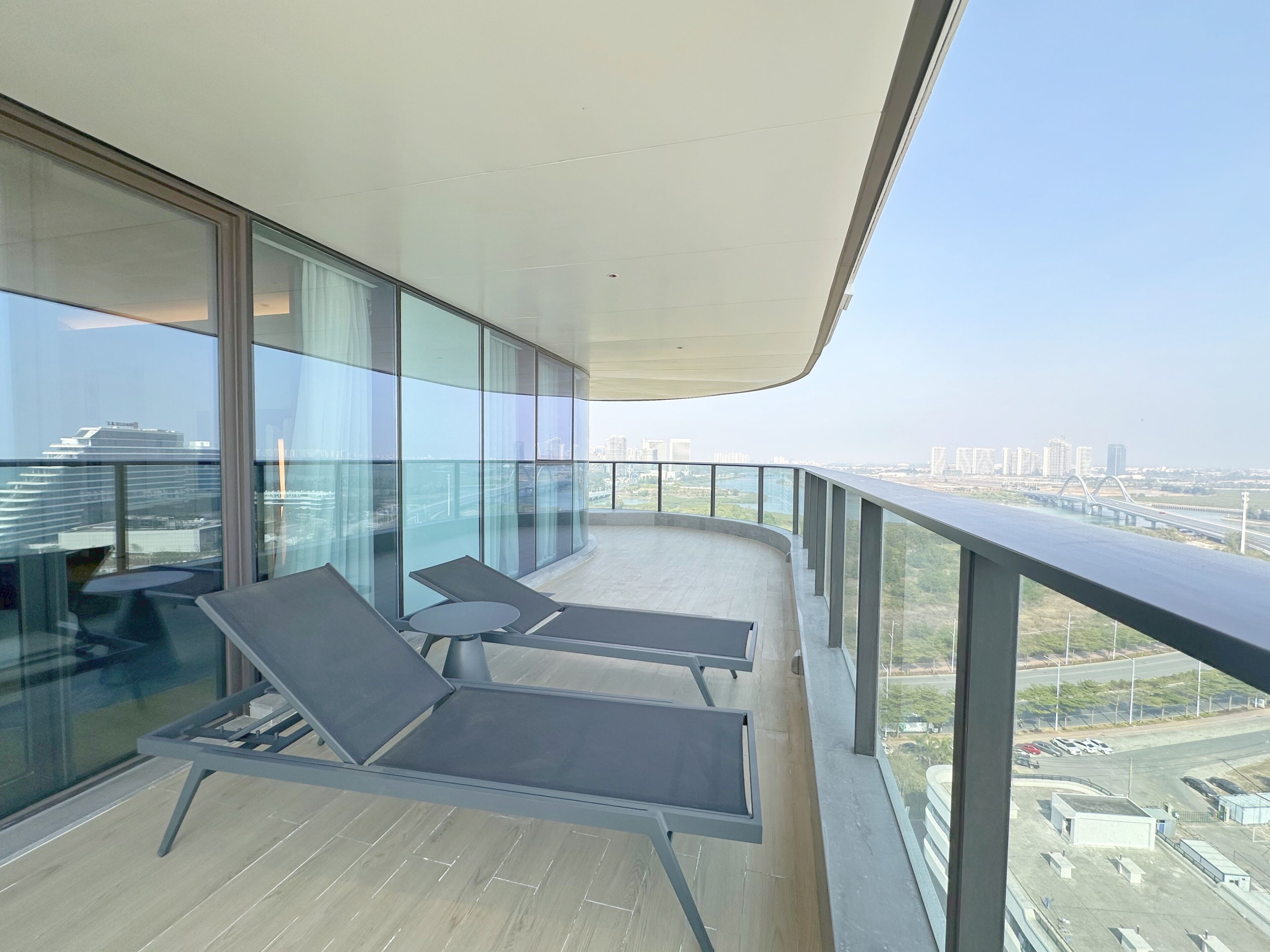 A balcony with two lounge chairs, a glass wall, and a view of a cityscape.