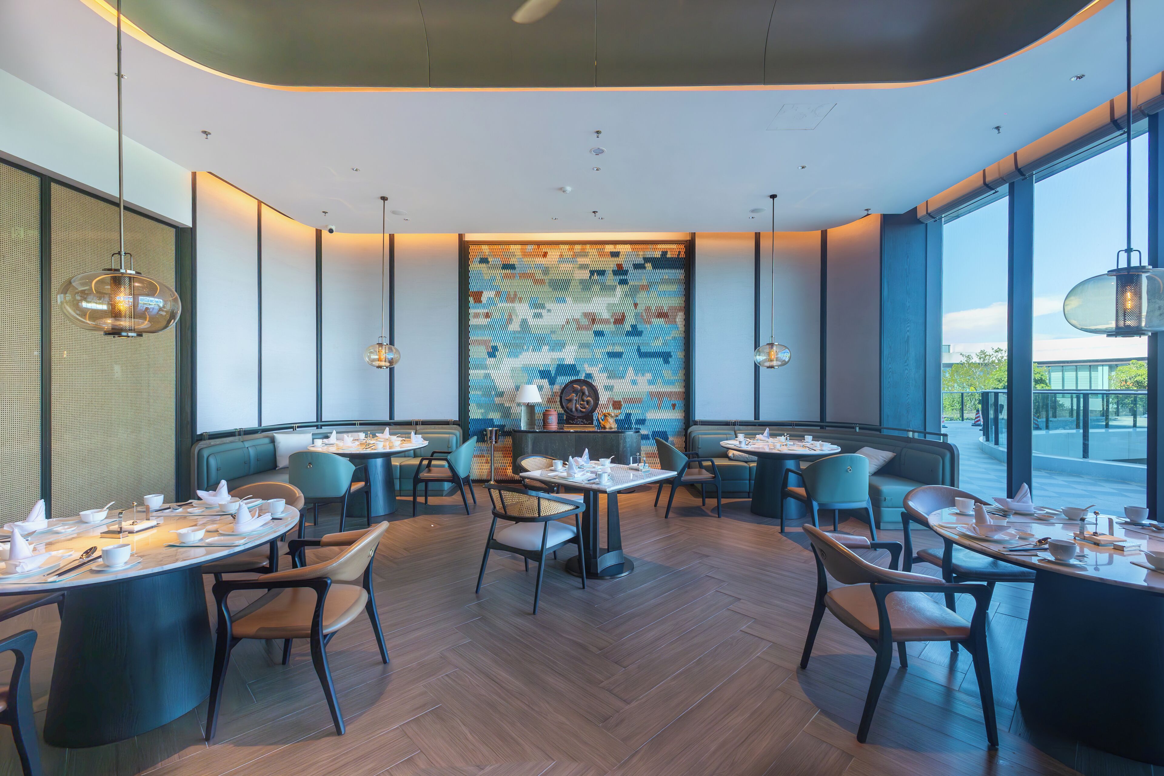 Un intérieur de restaurant moderne avec des tables rondes, des sièges rembourrés et un mur décoré de mosaïques.
