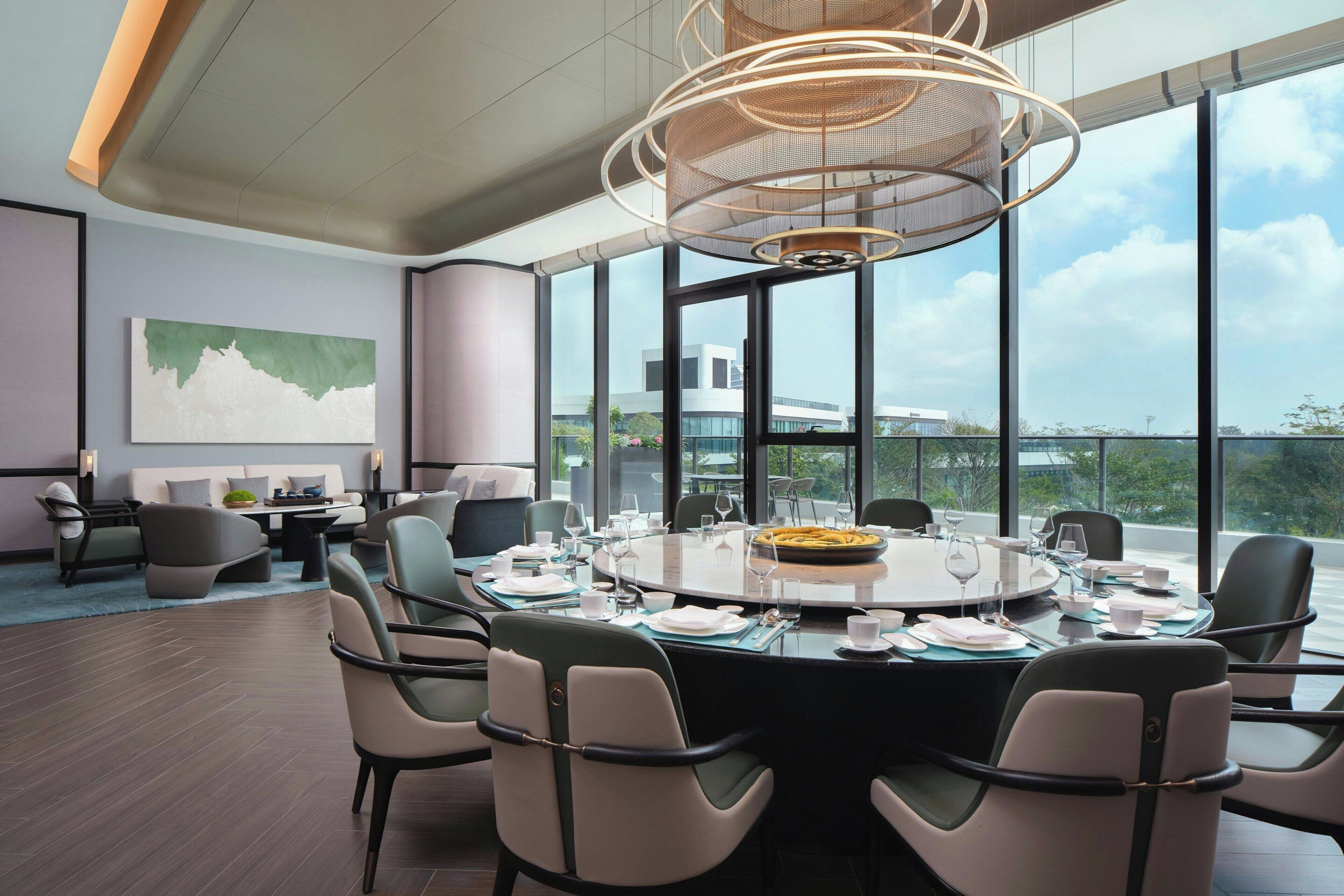 A modern dining area with a round table set for six, surrounded by chairs, and large windows offering a view of the cityscape.