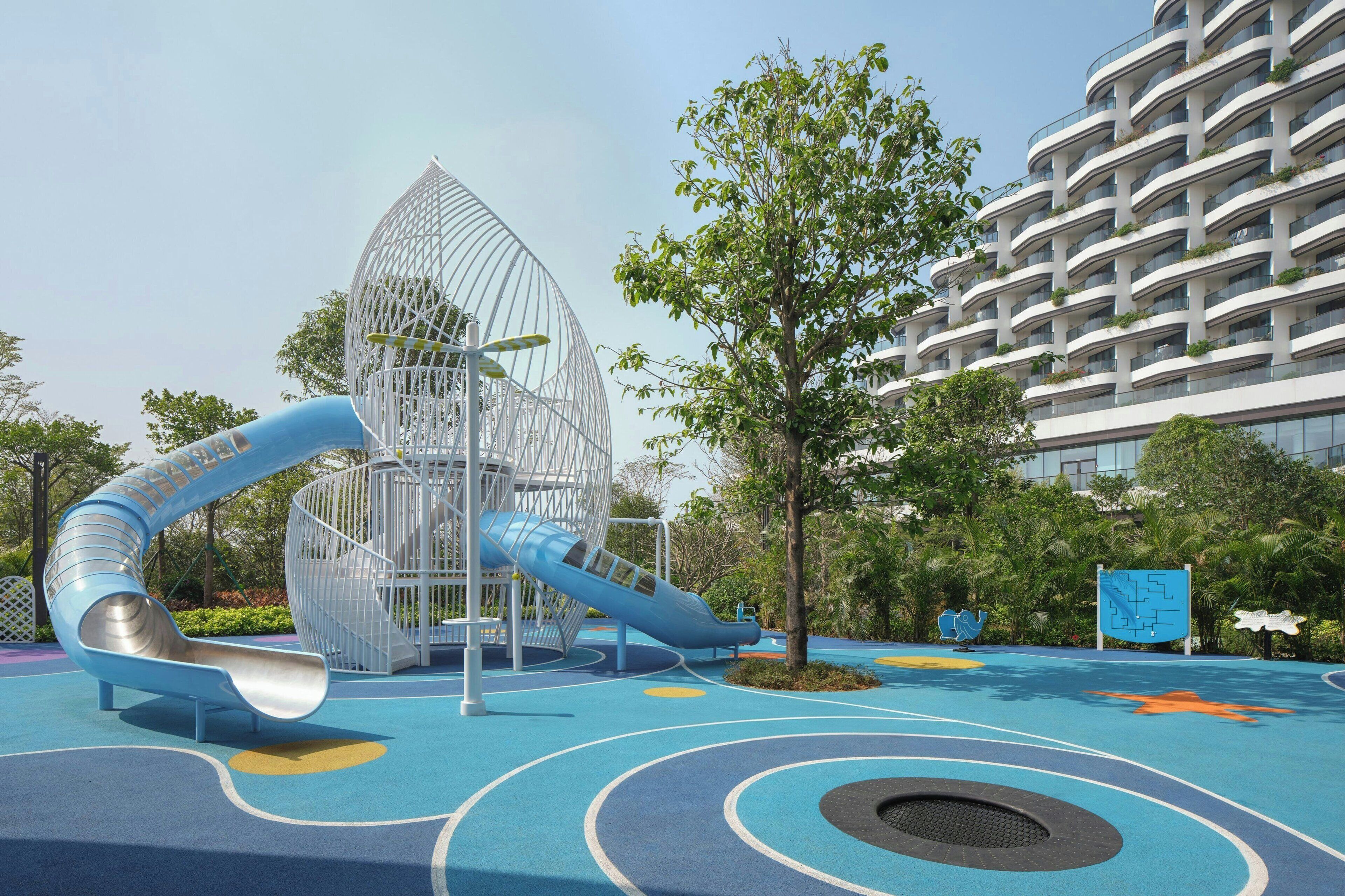 A playground with a slide and climbing structure, surrounded by trees and a building.