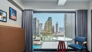 Een hotelkamer met een groot raam, een ronde tafel, een blauwe stoel en uitzicht op de stad.