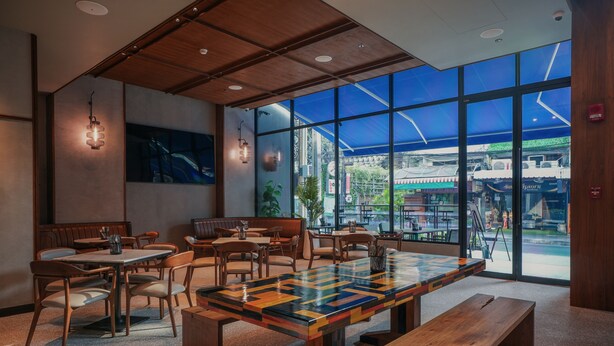 Ein modernes Restaurant mit Holzmöbeln, großen Fenstern und Blick auf die Straße.