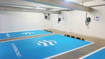 Un parking avec des places de stationnement bleues signalées par la mention « RESERVE AUX VEHICULES ELECTRIQUES » et une borne d’incendie fixée au mur.