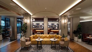 Een moderne lobby met een gele bank, twee kleine tafels en een kamerbreed tapijt met dessin.