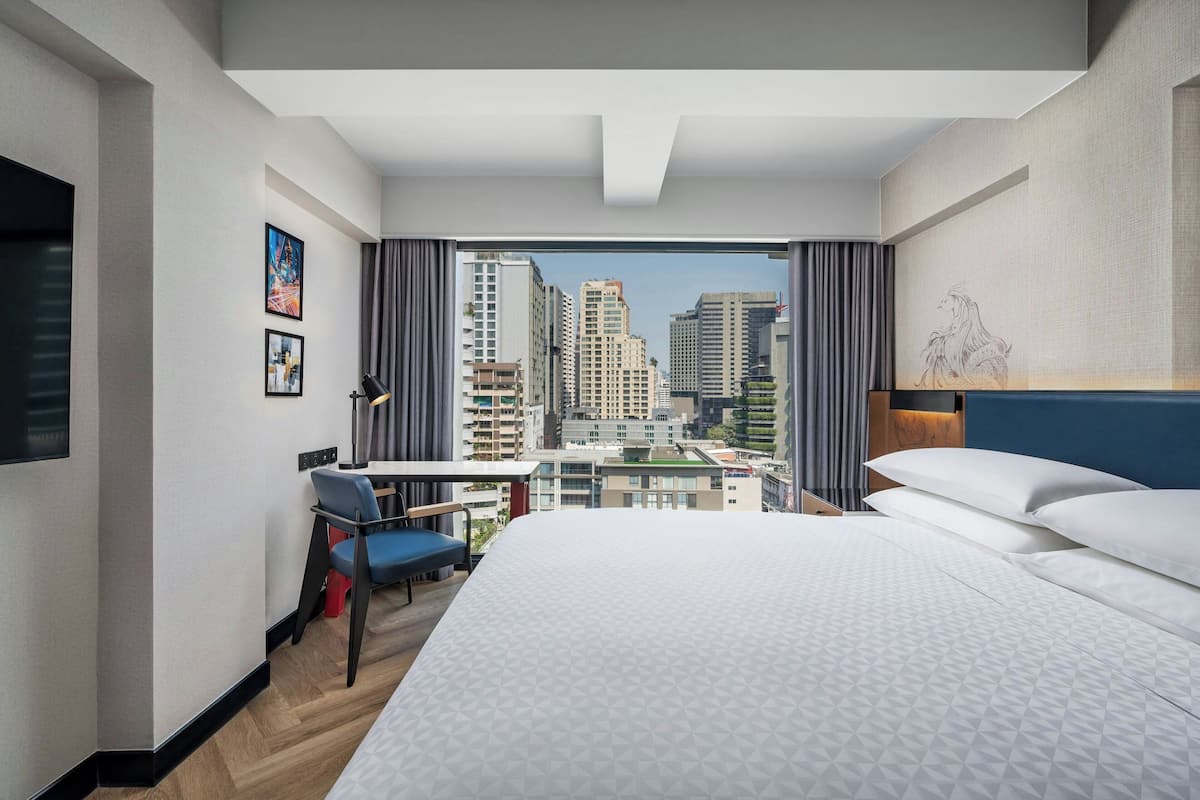 Una habitación de hotel con una cama grande, un escritorio con silla, televisión y vista a la ciudad.