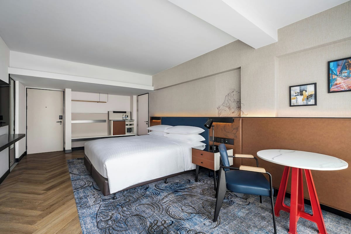 Una habitación de hotel moderna con una cama grande, un escritorio con silla, una mesita y un armario.