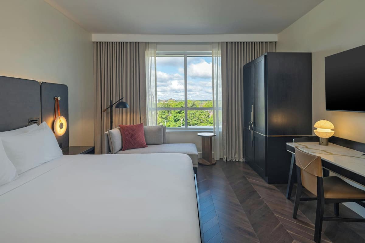 Een hotelkamer met twee bedden, een bureau, een televisie en een raam met uitzicht op groen.
