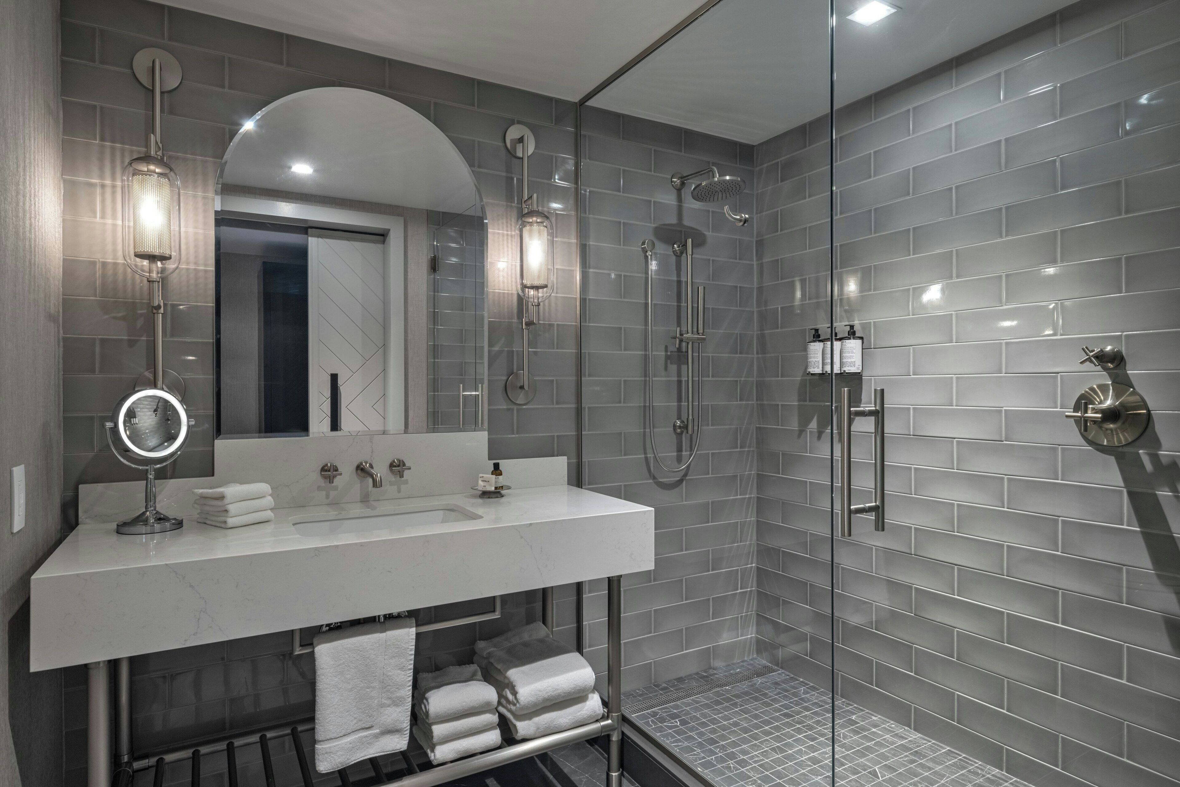 Une salle de bain moderne avec une douche à parois de verre, un meuble-lavabo avec un miroir et des serviettes soigneusement pliées.
