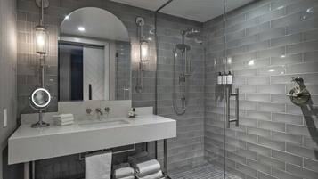 Een moderne badkamer met een douche in een glazen cabine, een wastafel met spiegel en netjes opgevouwen handdoeken.
