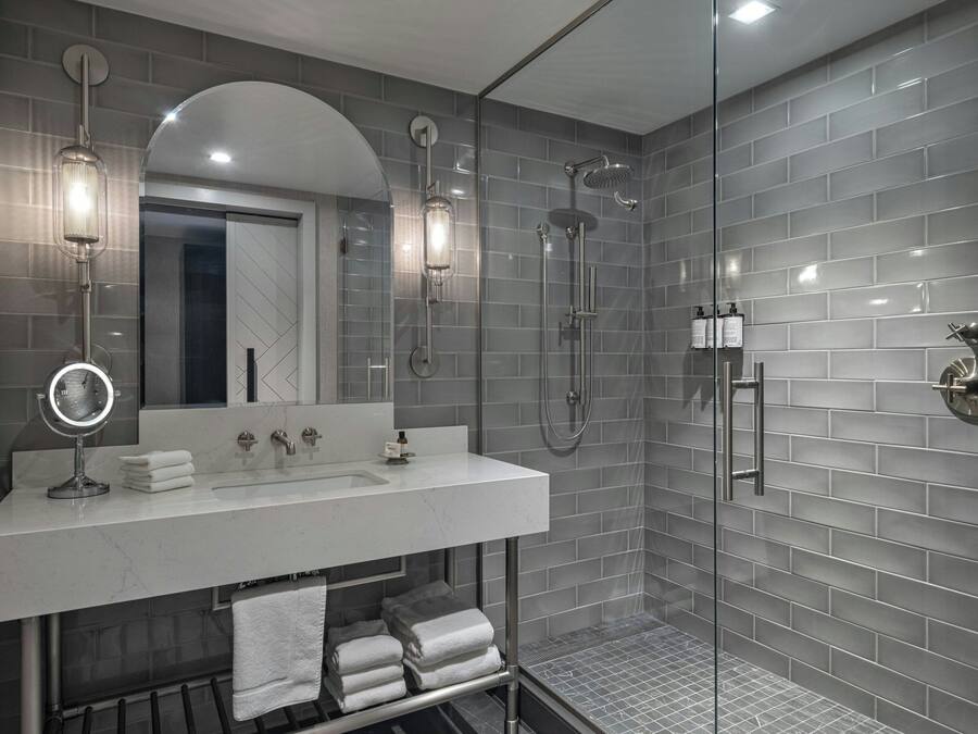 Een moderne badkamer met een douche in een glazen cabine, een wastafel met spiegel en netjes opgevouwen handdoeken.