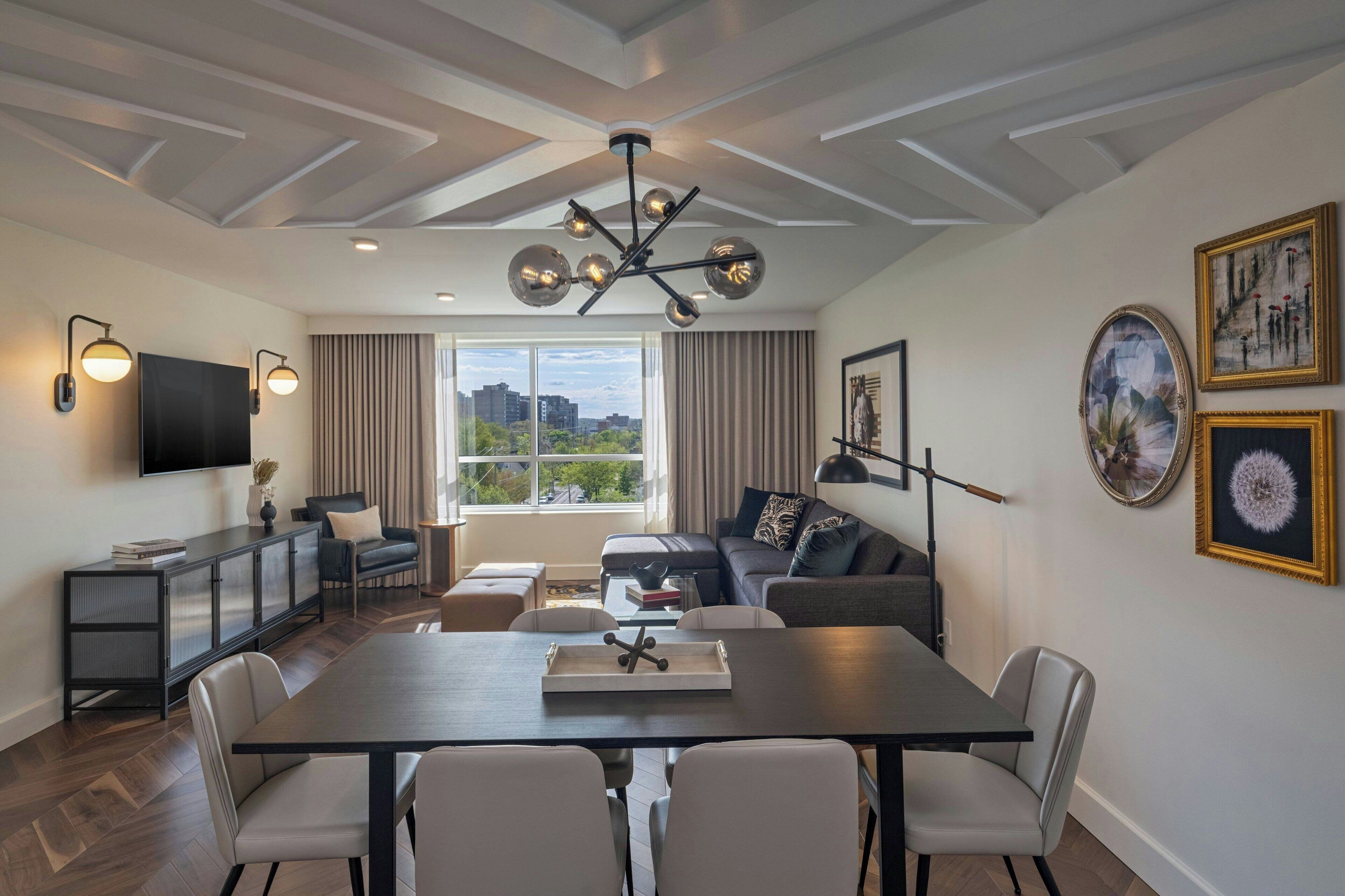 A modern living room with a dining area, a sofa set, a TV, and artwork on the walls.