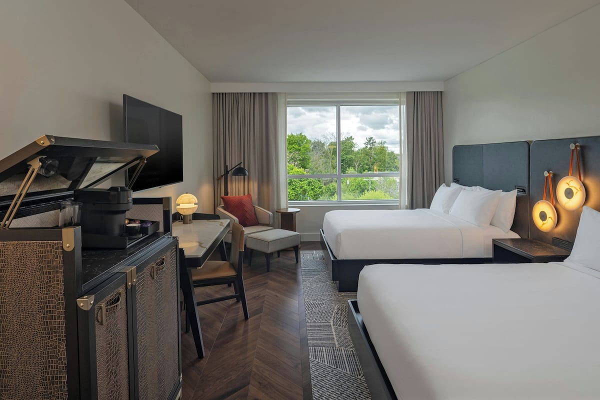 Hotelkamer met een piano, een televisie, twee bedden, een bureau, een stoel en een groot raam met uitzicht op groen.