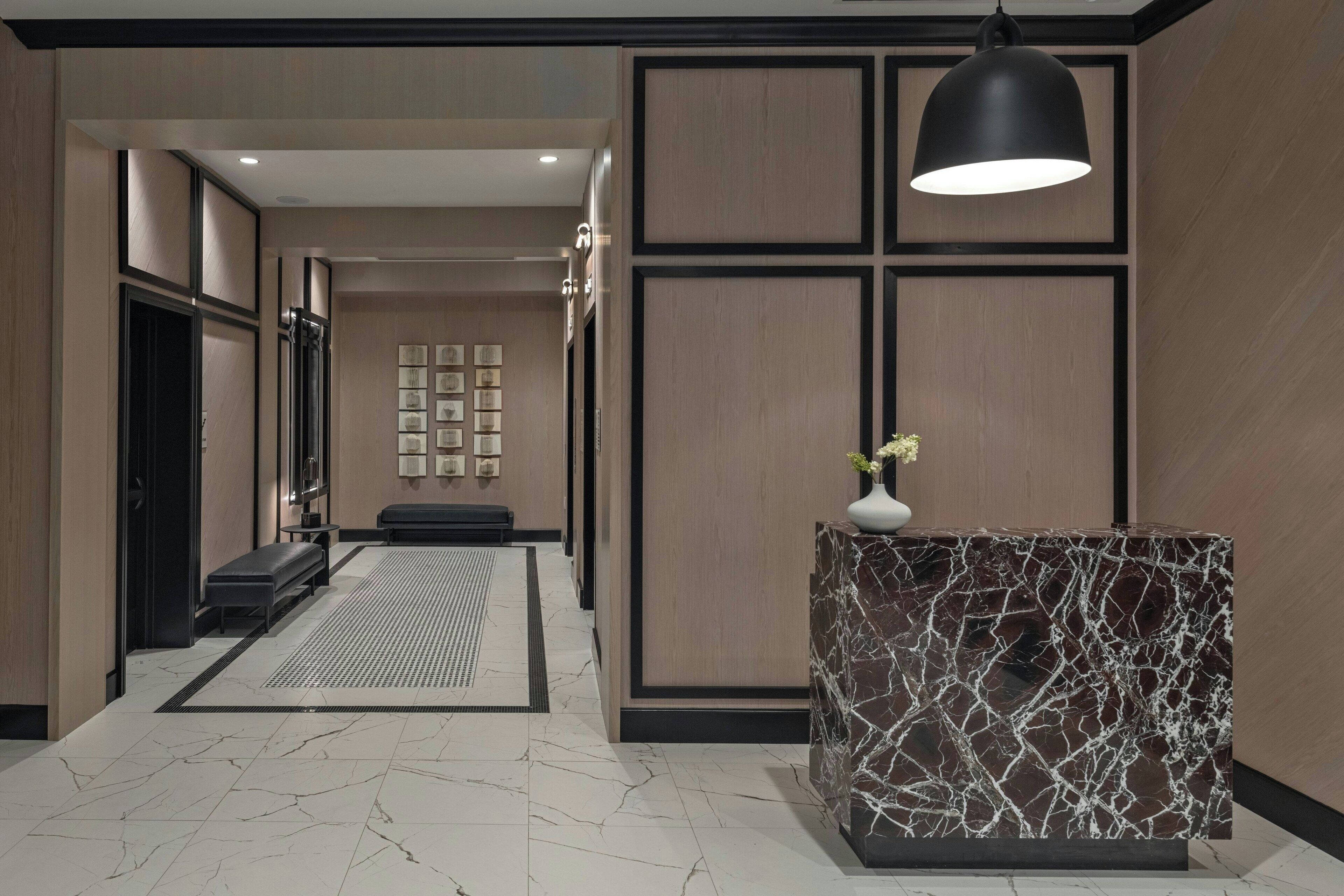 A modern lobby with a marble reception desk, a bench, and a patterned rug.