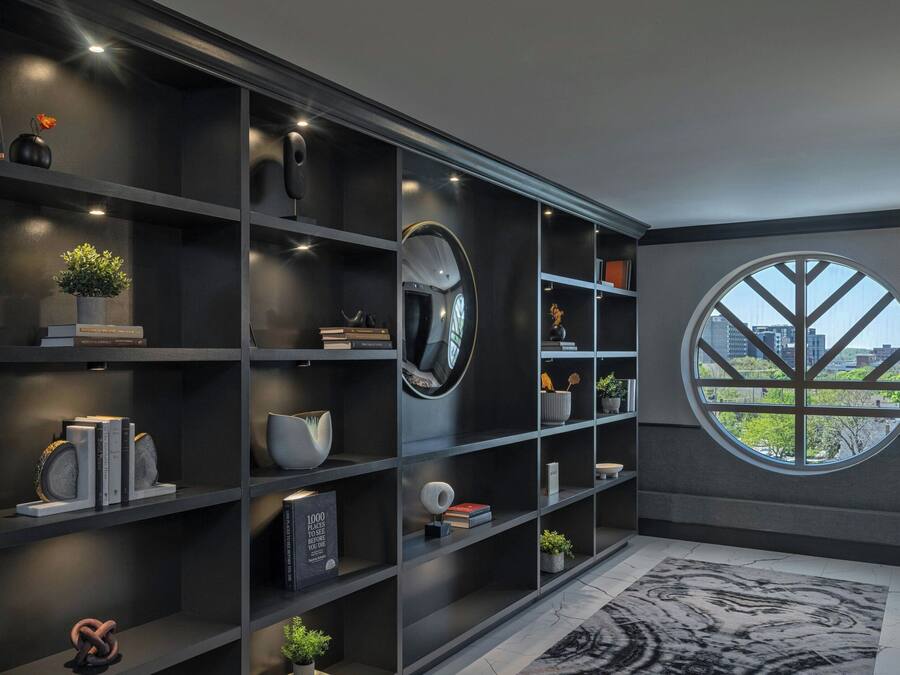 A modern interior with dark shelving, a large round window, and a view of the cityscape.