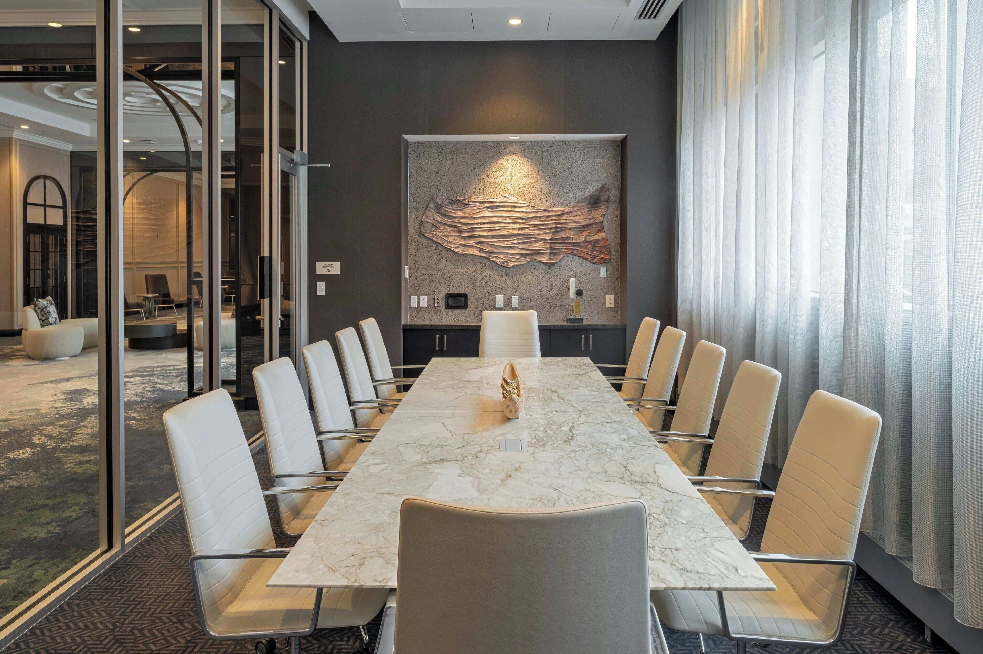 A conference room with a marble table, white leather chairs, and a large abstract painting on the wall.