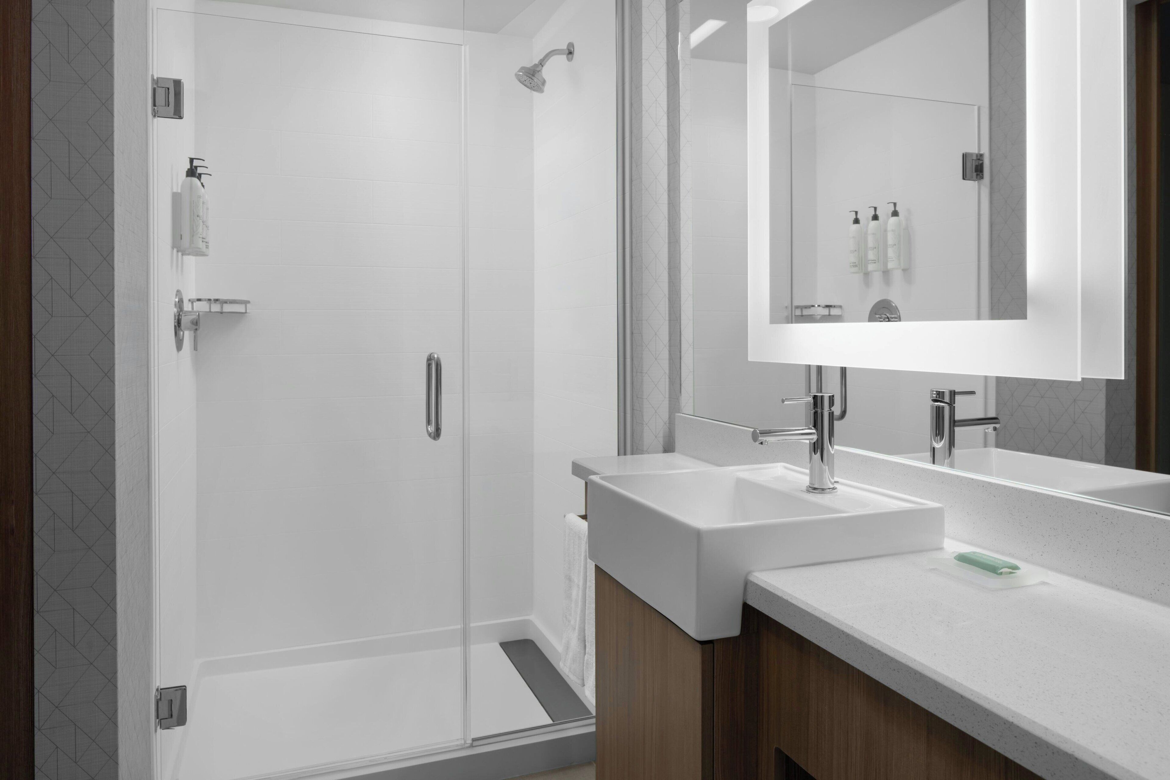 Ein modernes Badezimmer mit einer gläsernen Dusche, zwei Waschbecken und einem großen Spiegel.