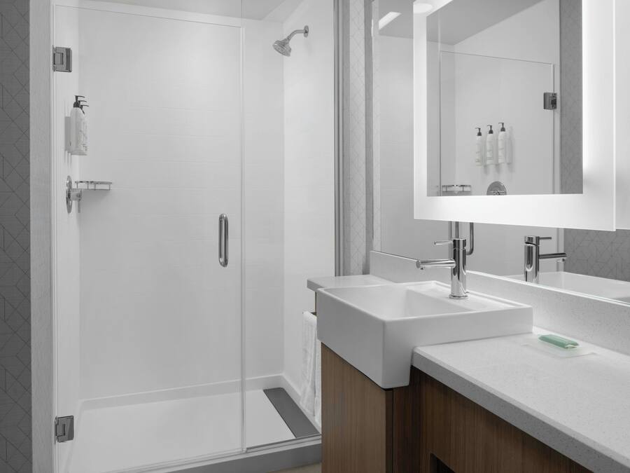 Un baño moderno con cabina de ducha de vidrio, dos lavamanos y un espejo grande.