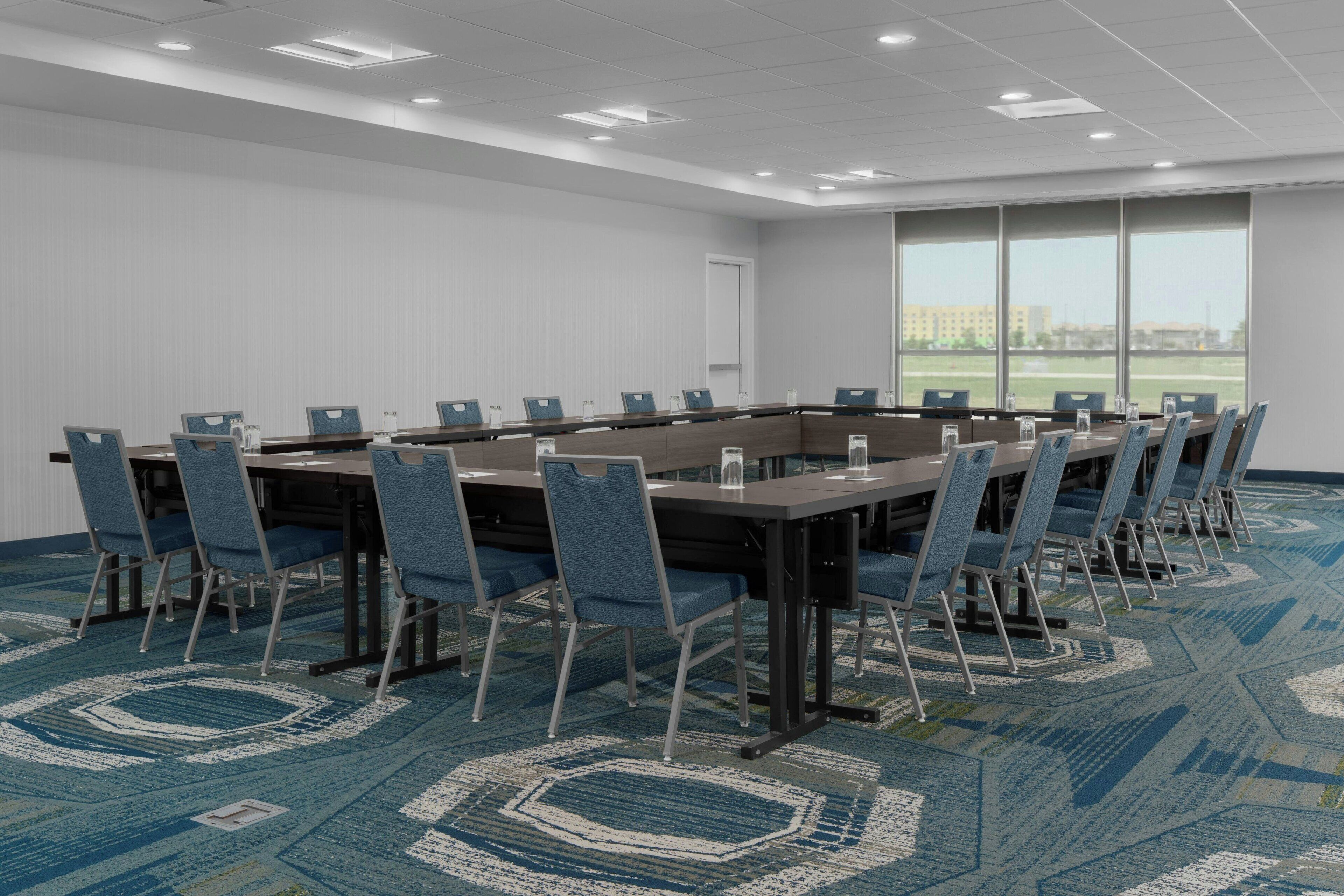 Une salle de conférence avec une longue table, des chaises bleues et un tapis à motifs.