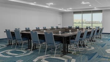 Une salle de conférence avec une longue table, des chaises bleues et un tapis à motifs.