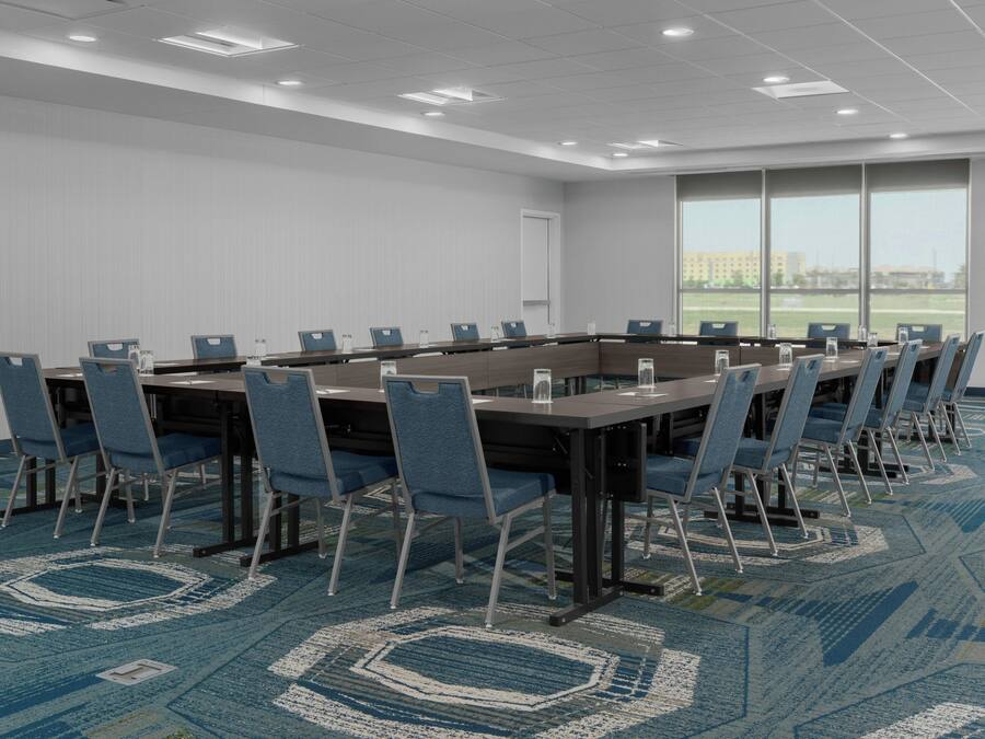Une salle de conférence avec une longue table, des chaises bleues et un tapis à motifs.