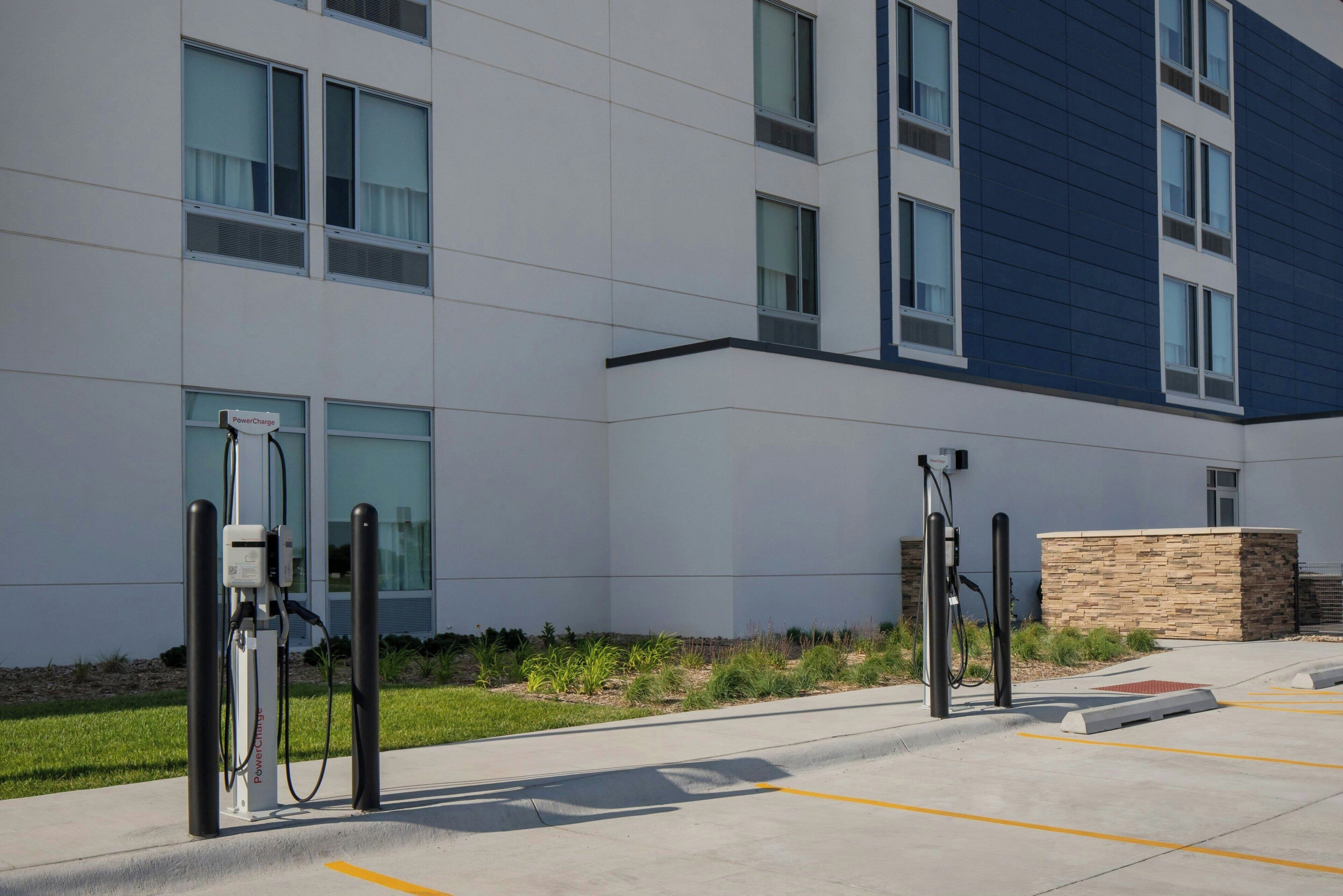 Um edifício moderno com área de estacionamento, estações de carregamento para veículos elétricos e um jardim ajardinado.