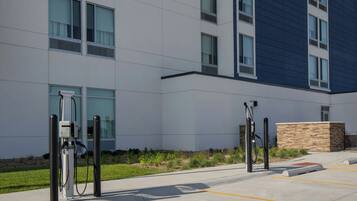 Um edifício moderno com área de estacionamento, estações de carregamento para veículos elétricos e um jardim ajardinado.