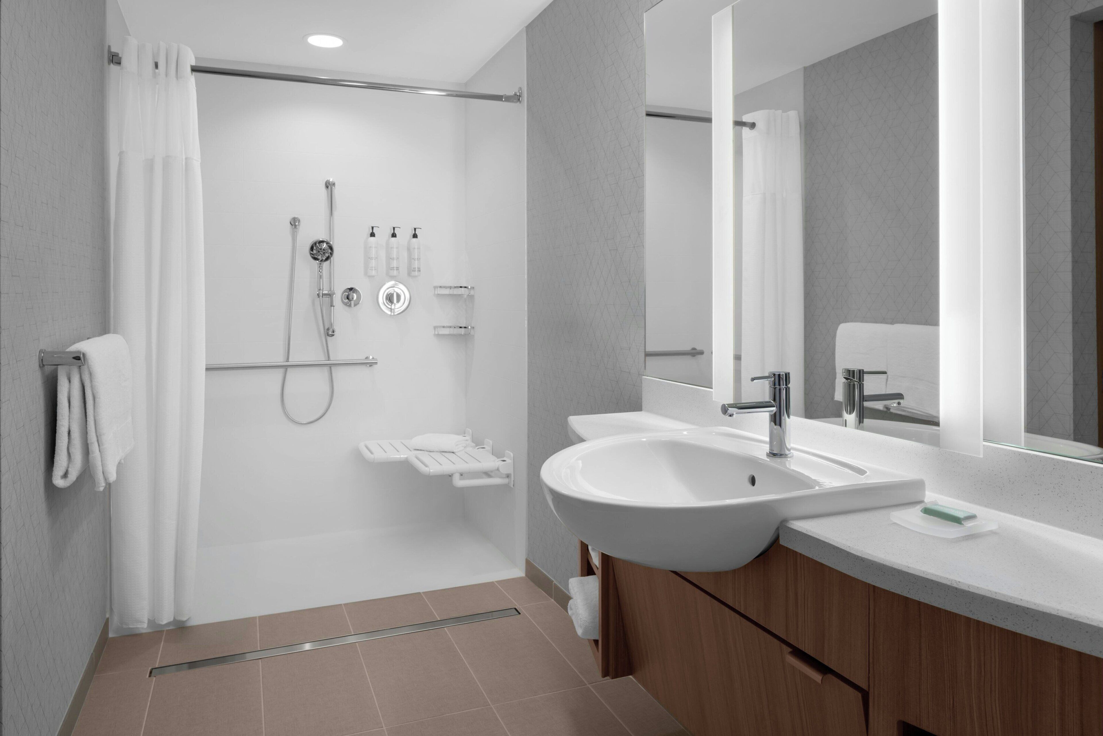 Ein modernes Badezimmer mit barrierefreier Dusche, großem Waschbecken und Spiegel.
