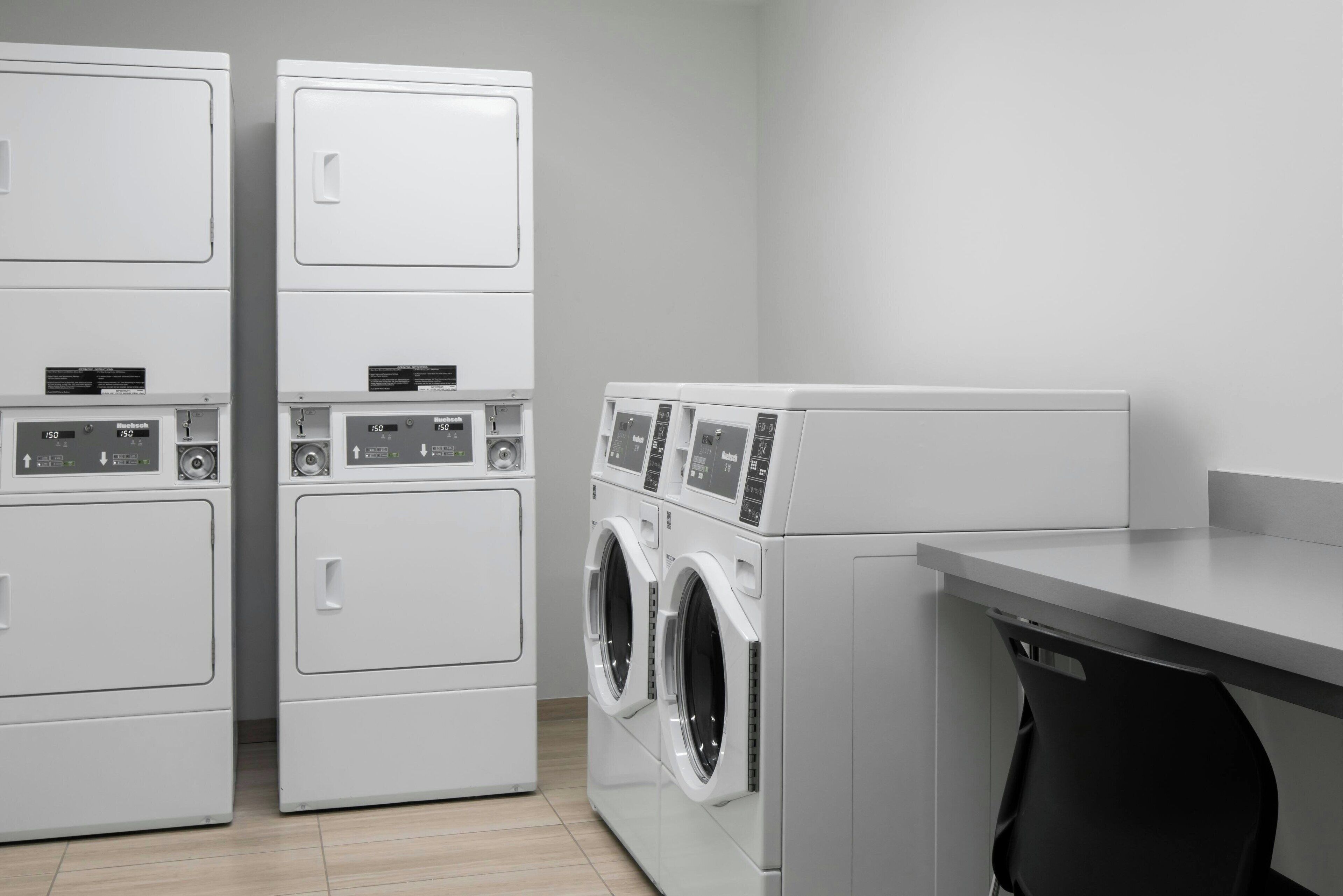 A laundry room with stacked washers and dryers, a countertop, and a black trash bin.