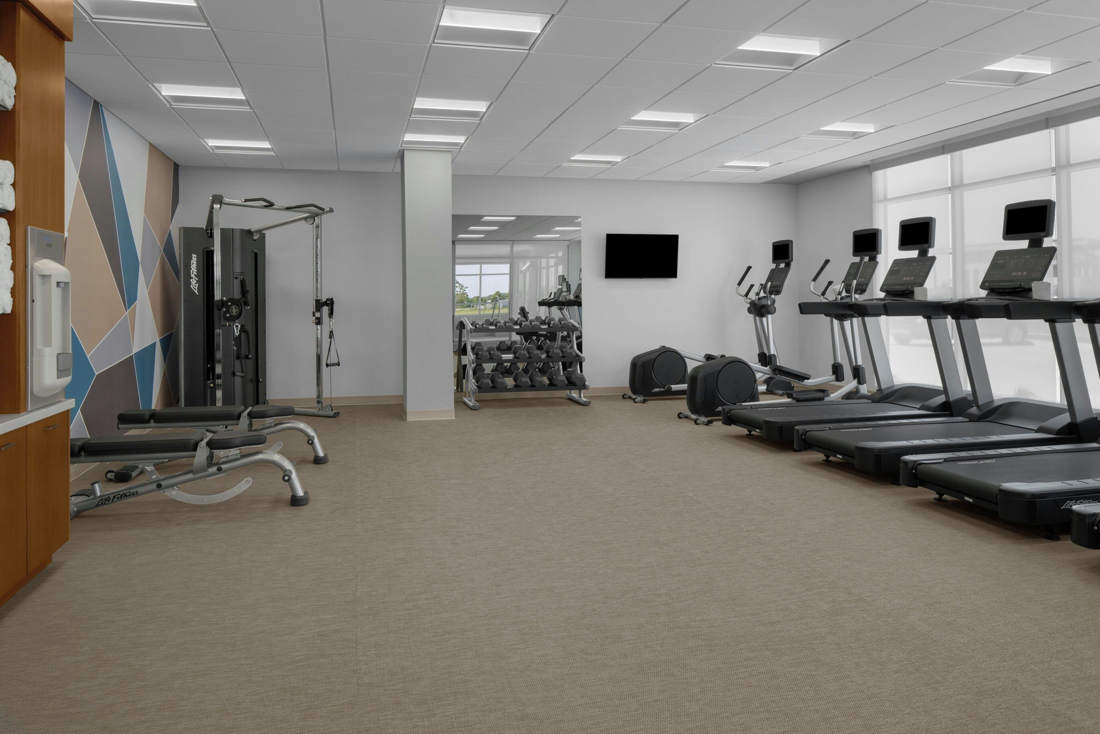 Une salle de sport équipée de tapis de course, d’appareils de musculation et d’haltères.