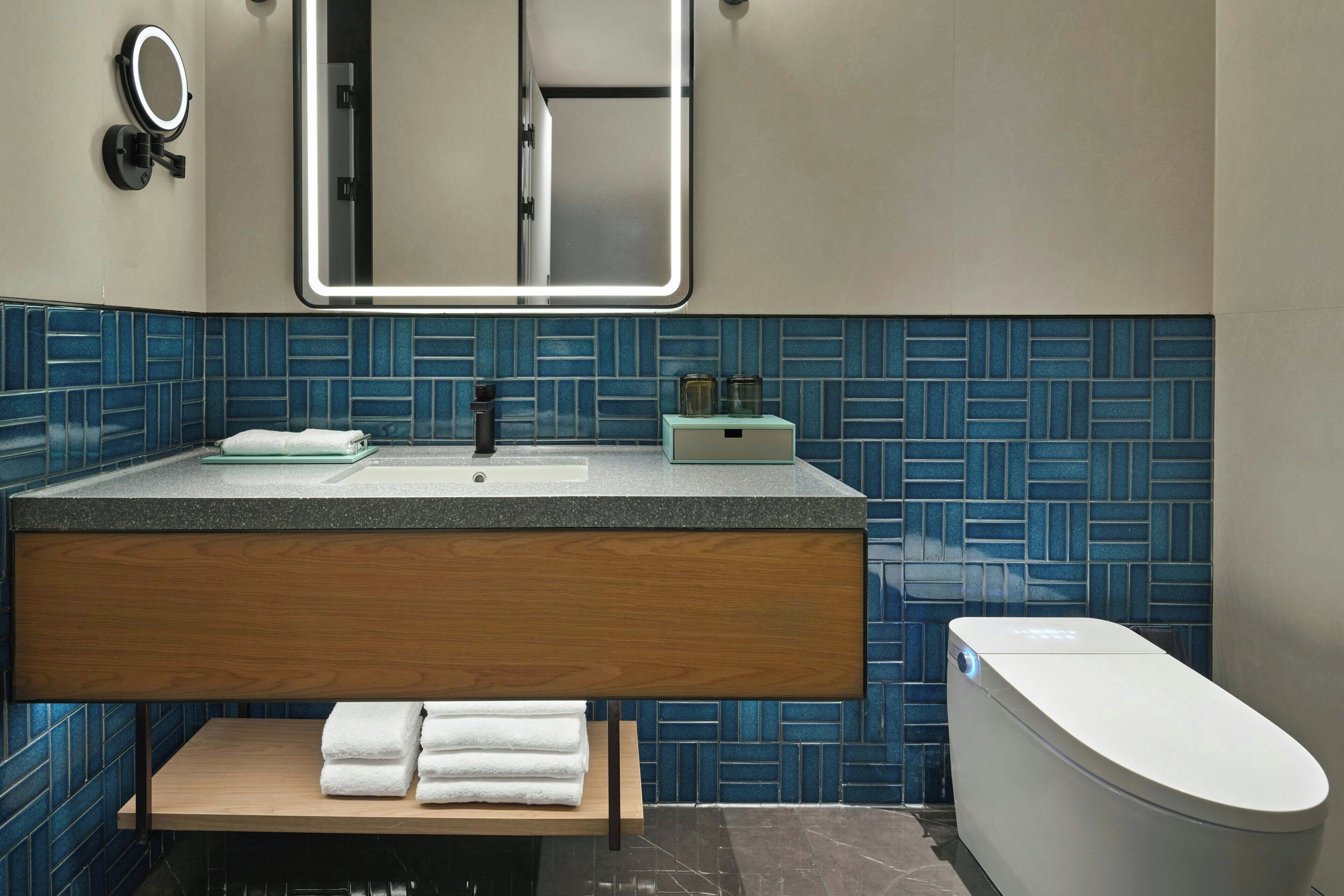 A modern bathroom with a wooden vanity, a sink, a mirror, and a toilet.
