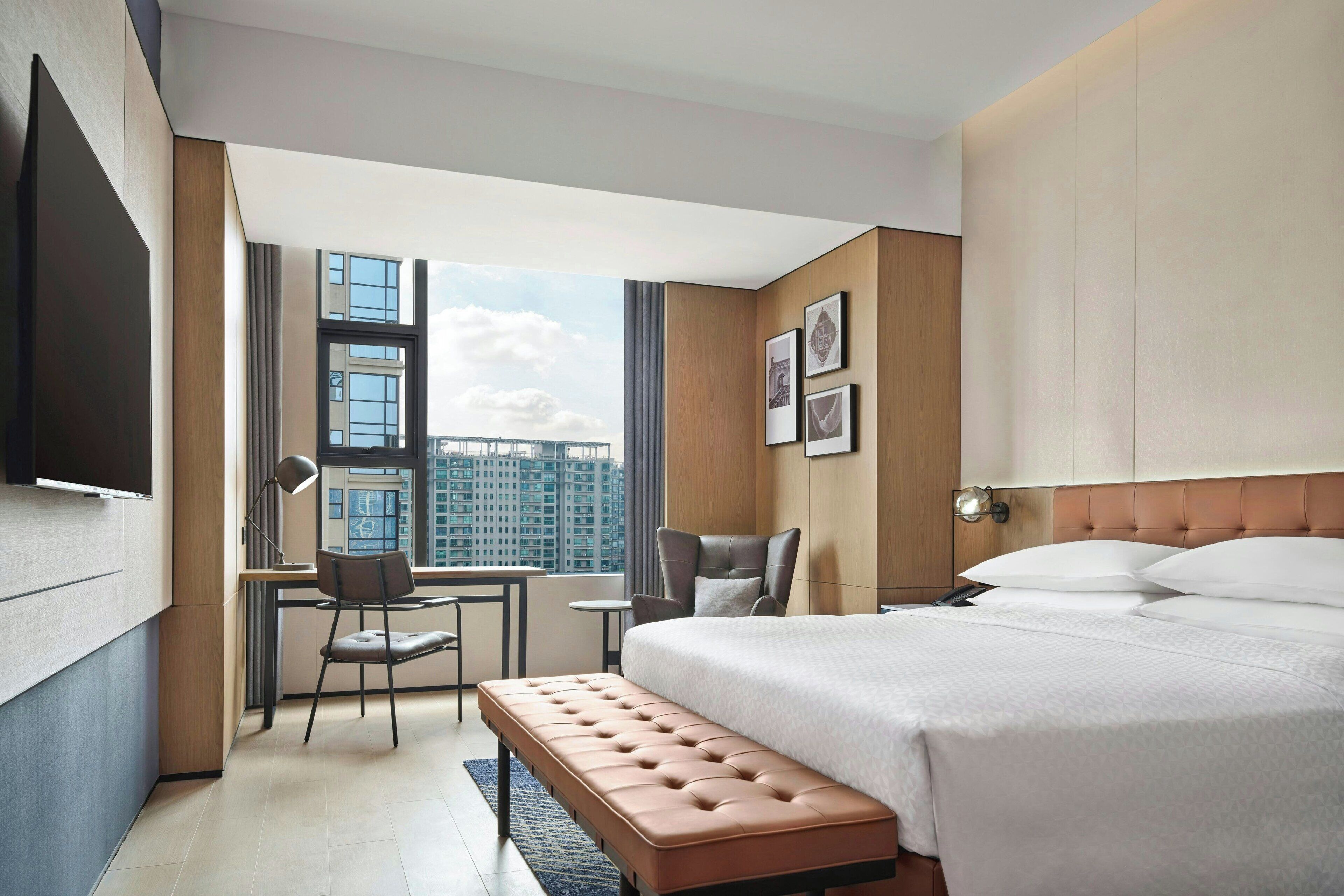 Ein modernes Hotelzimmer mit einem großen Bett, einem Schreibtisch, einem Sessel und Blick auf die Stadt.