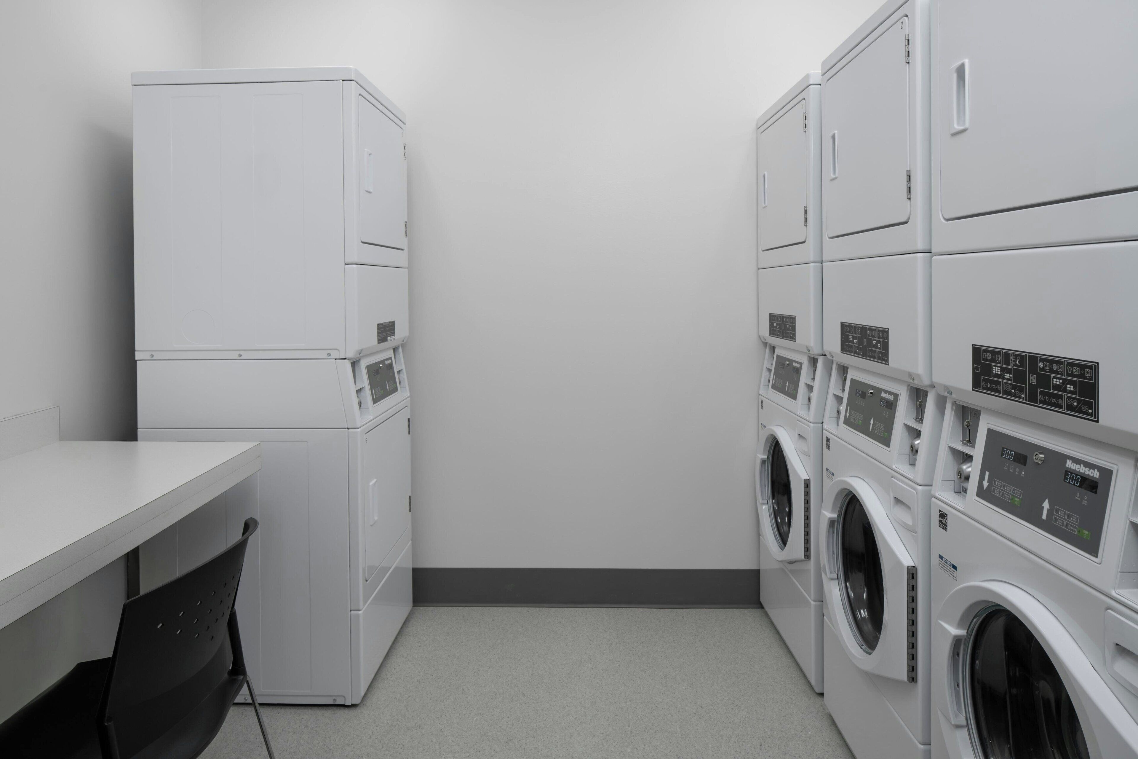 A laundry room with stacked washers and dryers, a table, and chairs.