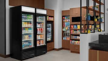 Una kitchenette con dos refrigeradores negros llenos de bebidas y aperitivos, armarios de madera y una encimera.