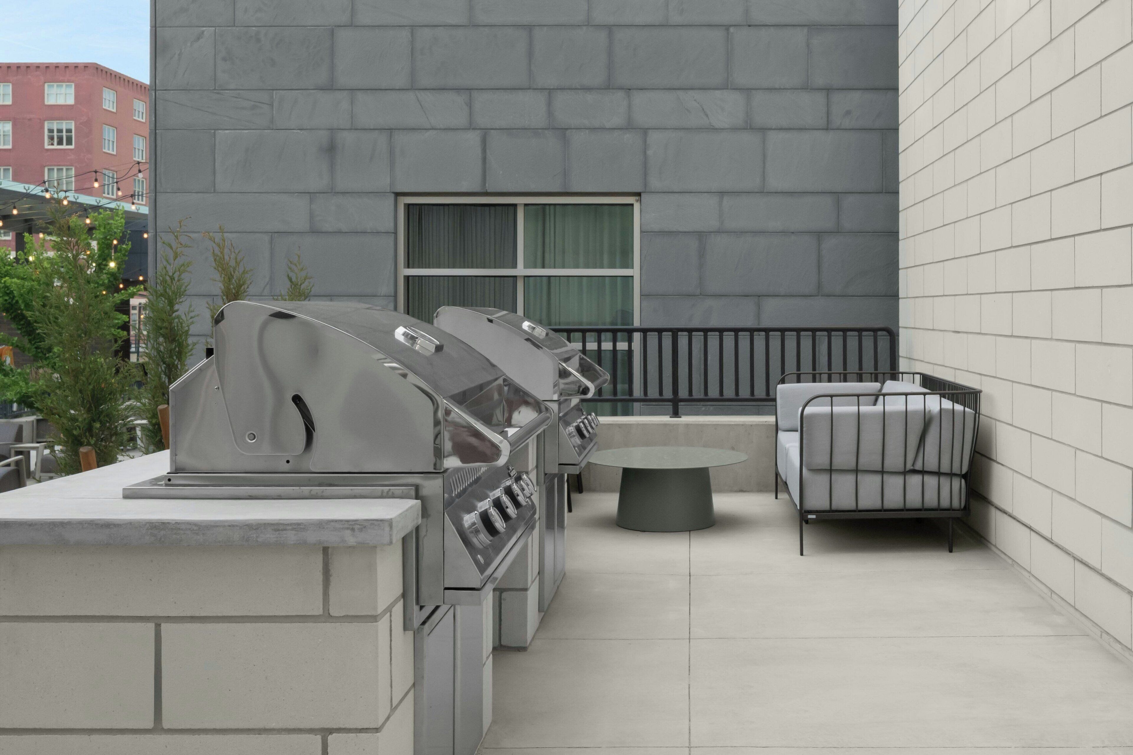 Une terrasse extérieure équipée d’un barbecue, d’une table ronde et d’un canapé.