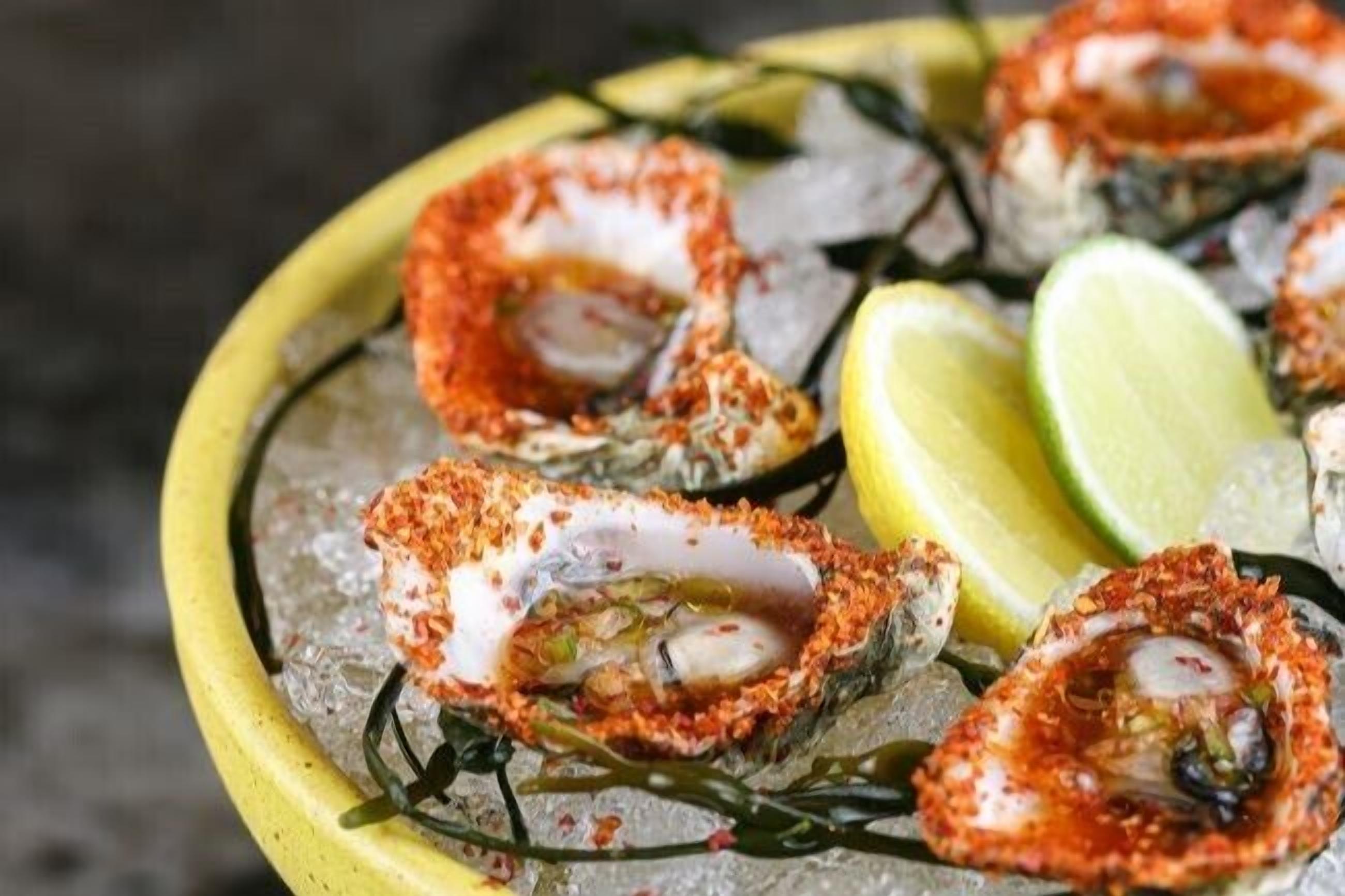 A plate of seafood, specifically oysters, seasoned with spices and served on ice with lemon wedges.