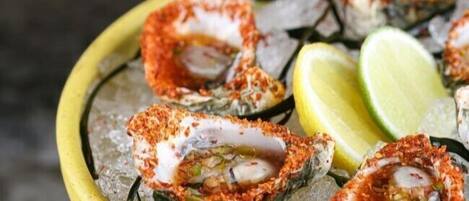 A plate of seafood, specifically oysters, seasoned with spices and served on ice with lemon wedges.