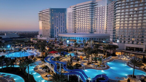 Un hotel con una gran piscina, varias toboganes de agua y un área exterior bien iluminada con sillones y sombrillas.