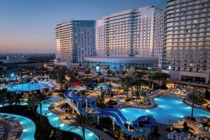 Un hotel con una gran piscina, varias toboganes de agua y un área exterior bien iluminada con sillones y sombrillas.