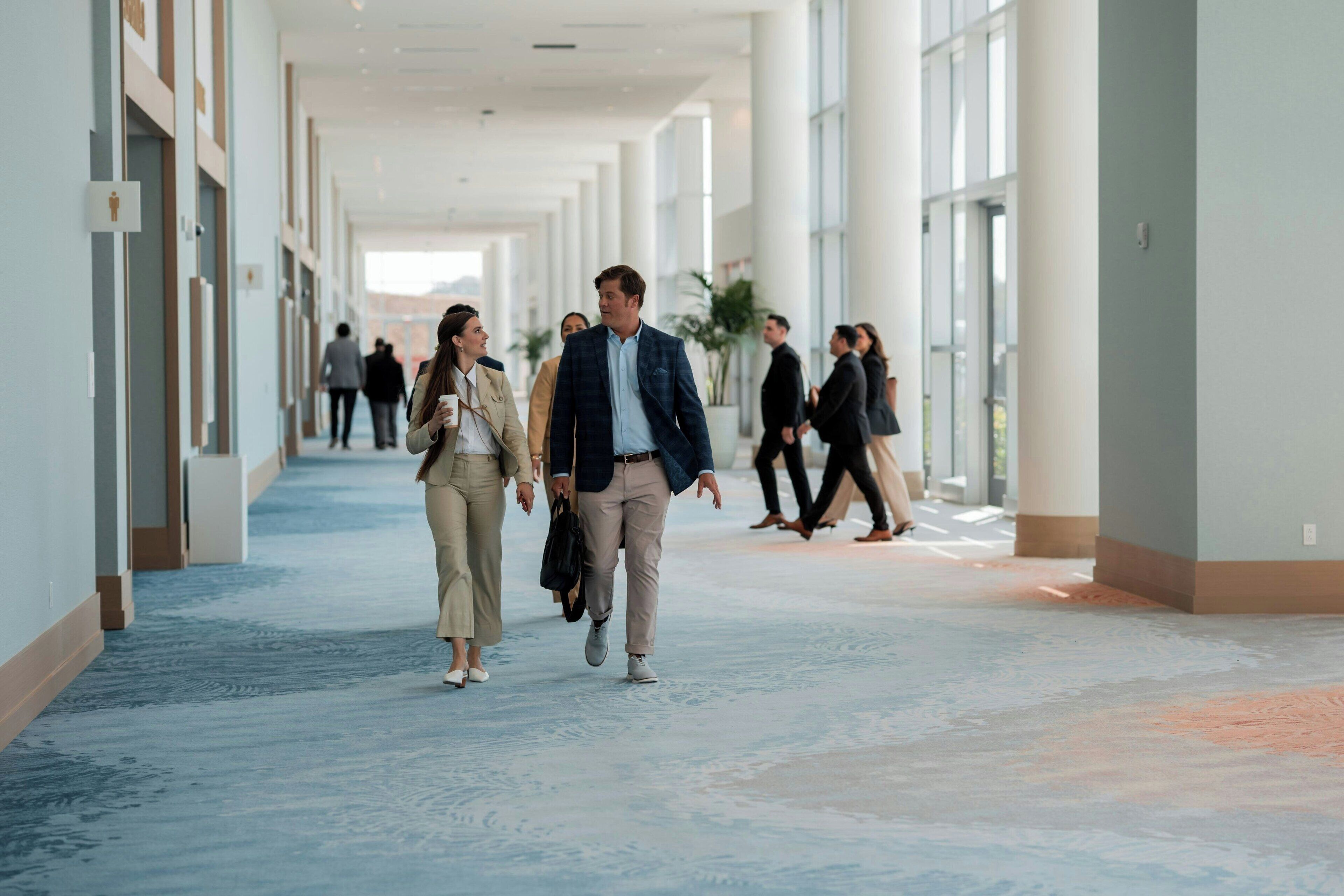 A spacious corridor with a blue carpet, large windows, and a modern architectural design.