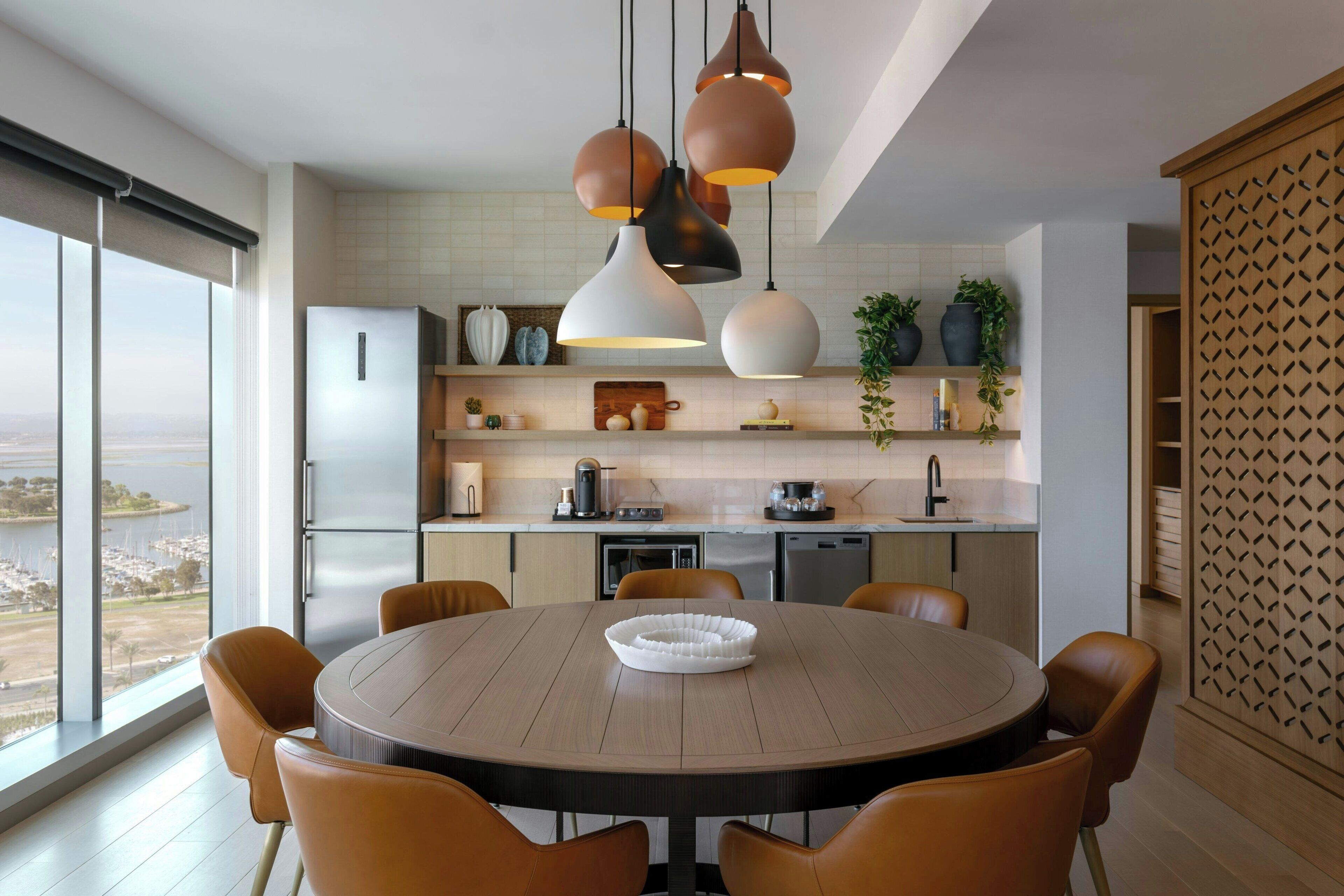 A modern kitchen with a round dining table, pendant lights, and a view of the city.