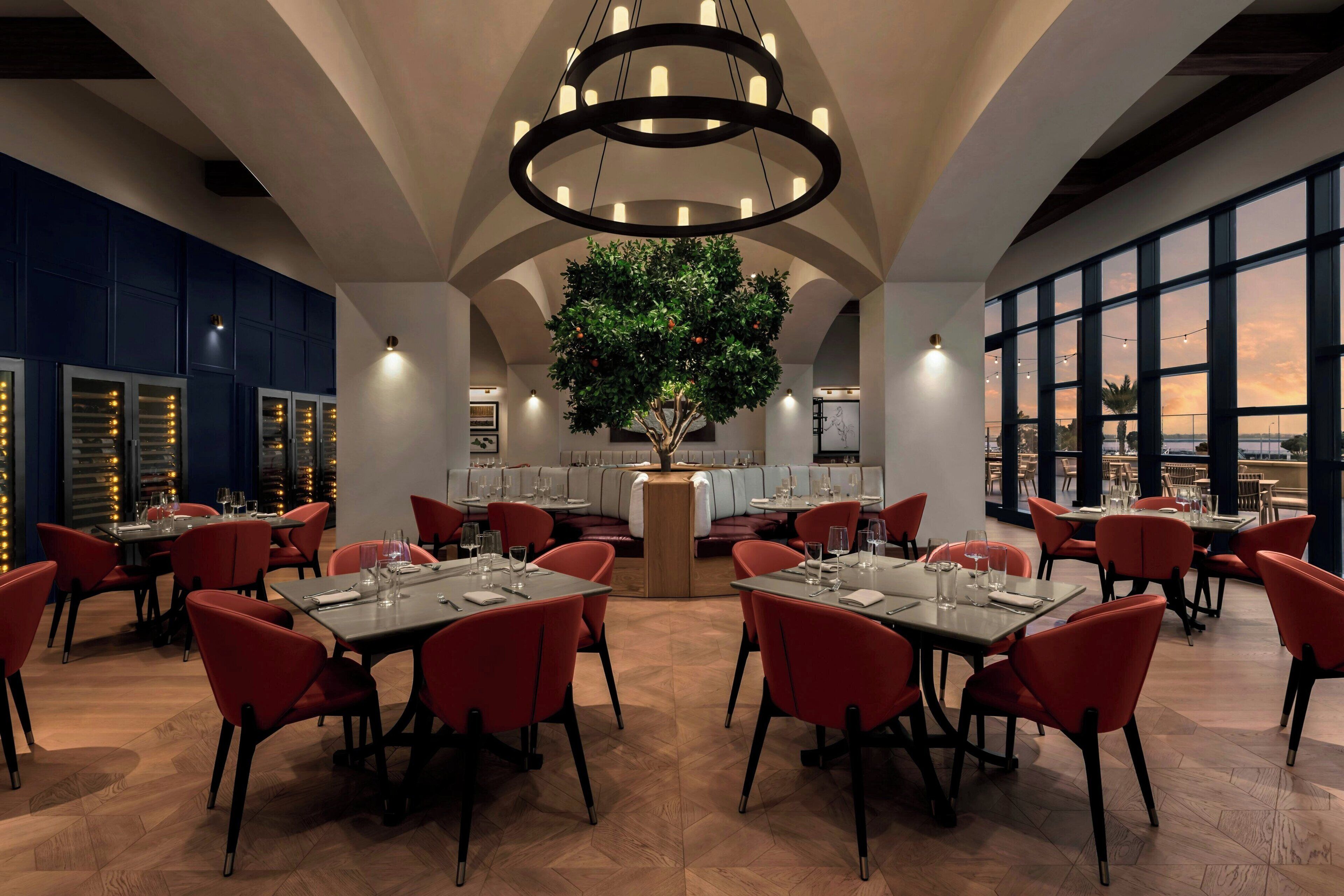 Un restaurante con mesas redondas, sillas rojas y un árbol en el centro.