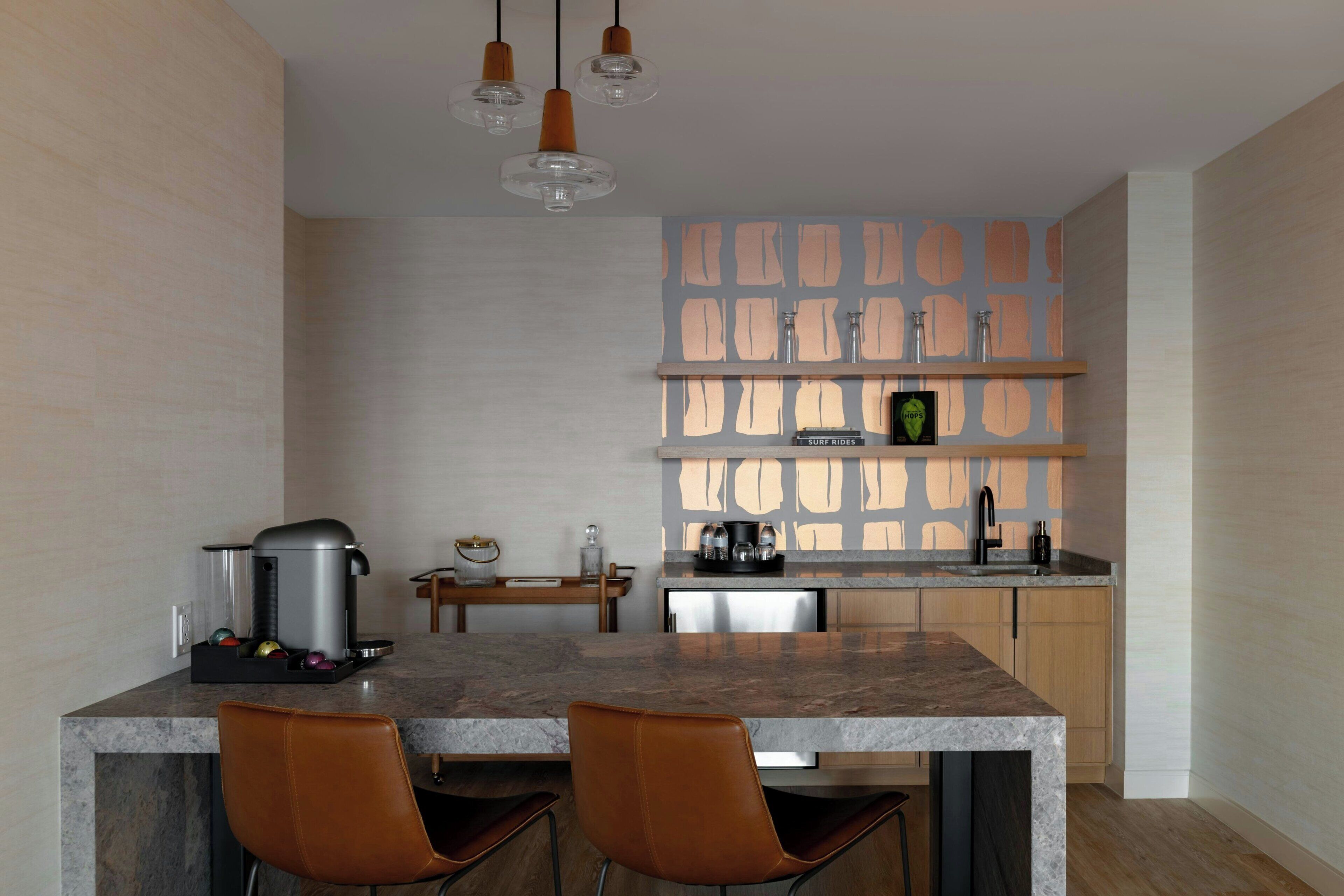 A modern kitchen with a marble countertop, two brown leather chairs, a coffee machine, and a coffee pot.
