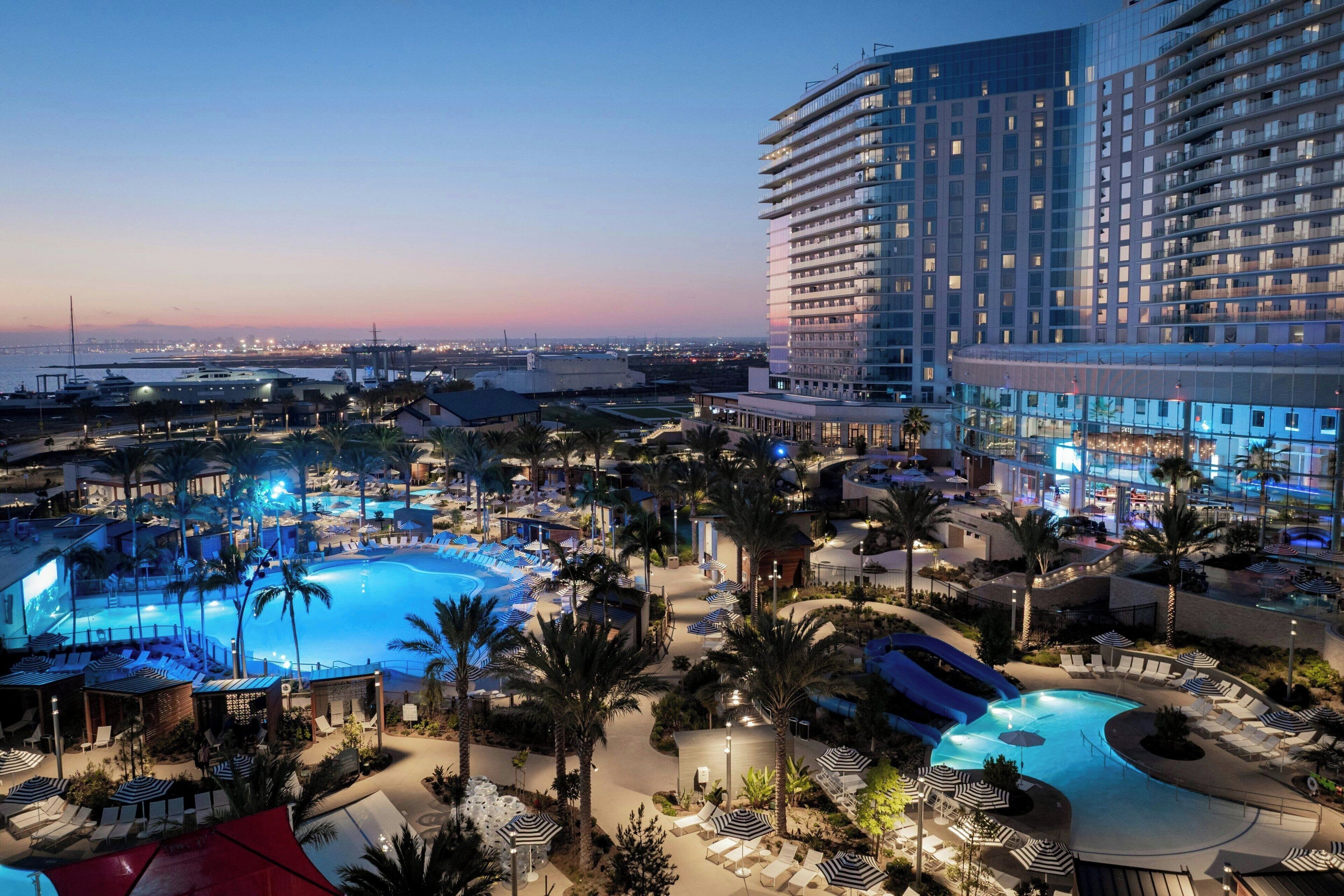 Ein Resort mit mehreren Schwimmbecken, Palmen und einem großen Hotelgebäude.