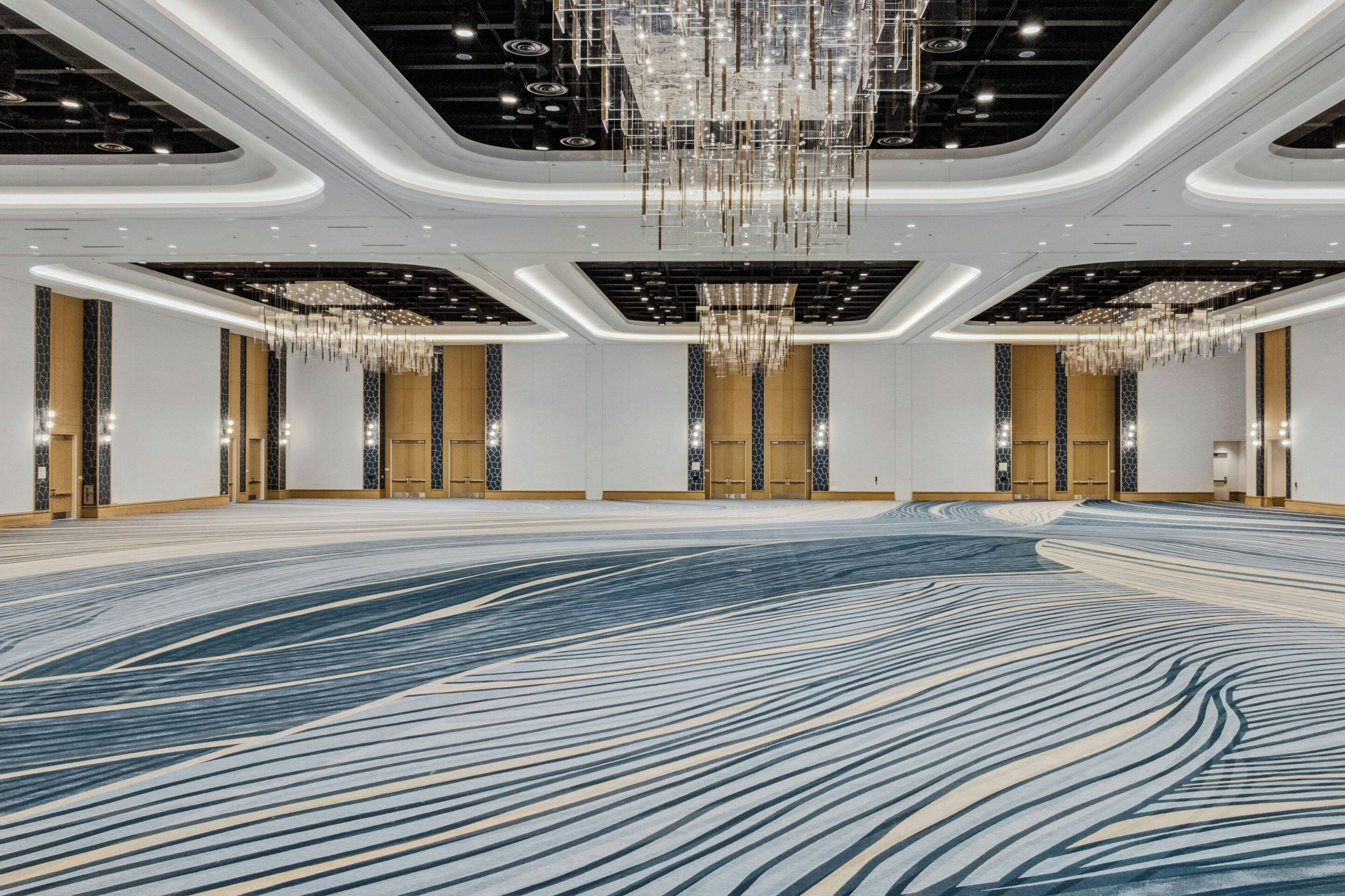 A spacious, modern hotel lobby with a large, patterned carpet, elegant chandeliers, and a clean, minimalist design.