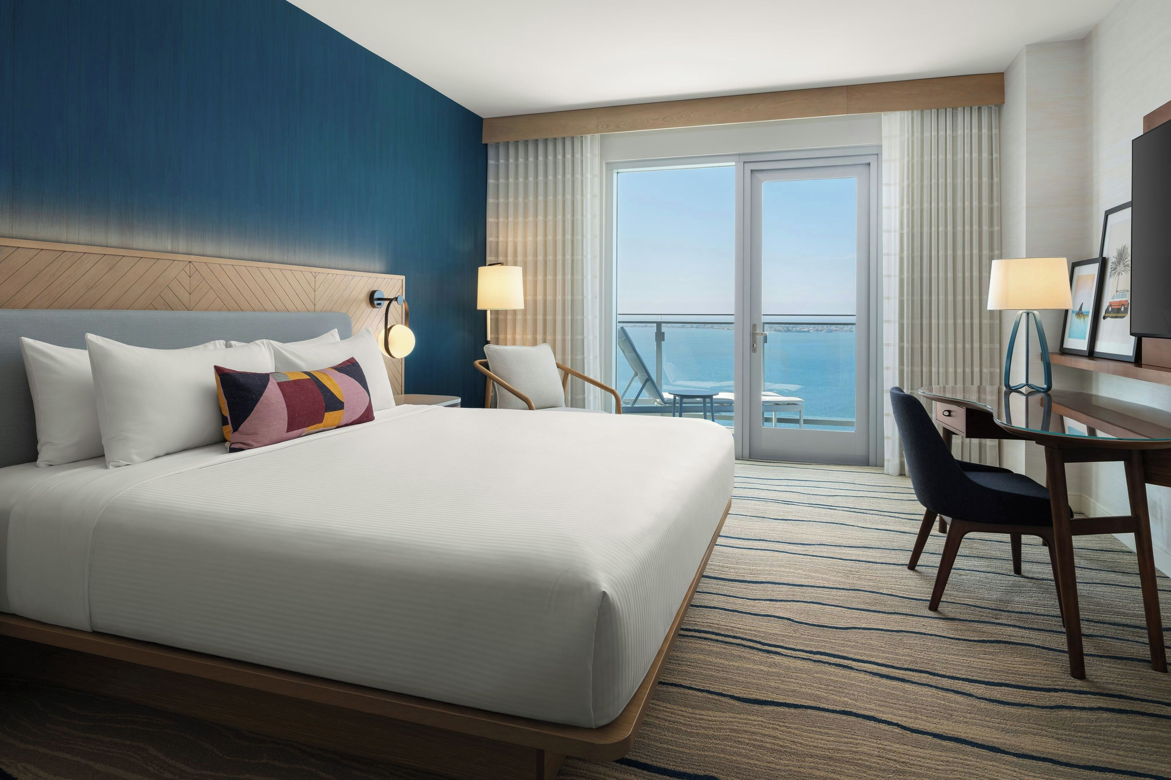 Ein Hotelzimmer mit einem großen Bett, einem Schreibtisch, einem Stuhl und Meerblick.