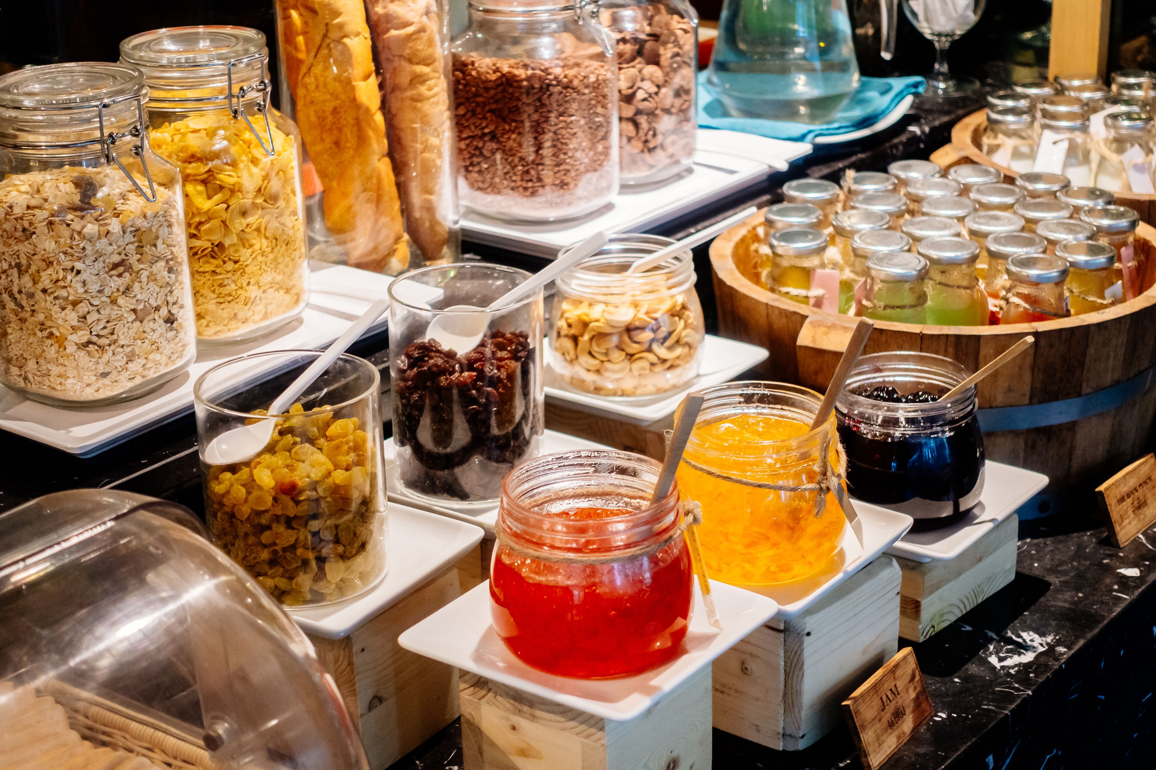A variety of food items in jars and containers, including cereals, nuts, and jams, displayed on a counter.