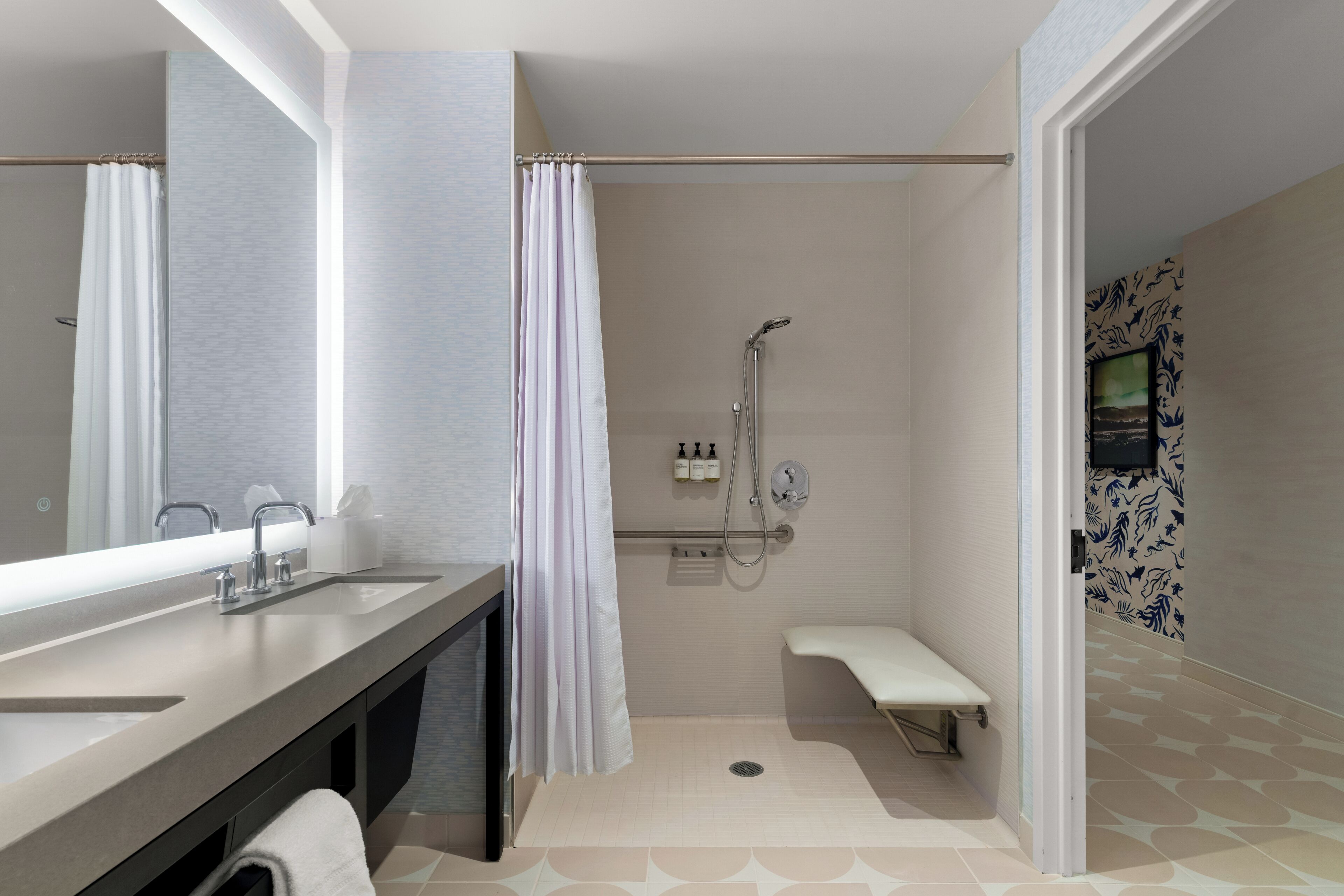 Un baño moderno con un espejo grande, un lavamanos, una ducha con cabezal de ducha manual y un banco.